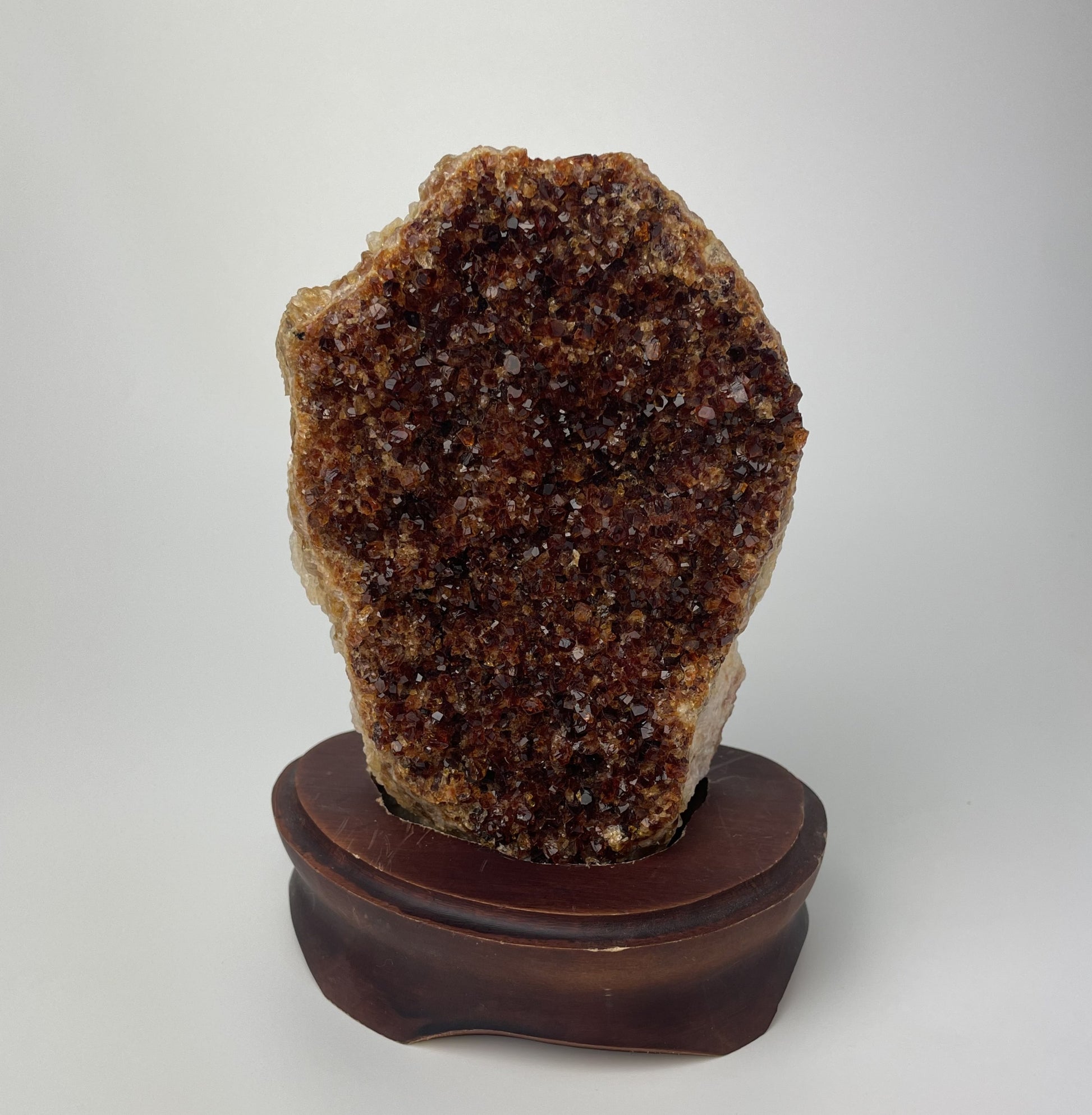 Citrine cluster with deep, orange-colored crystal formations on a wooden stand against a gray background.