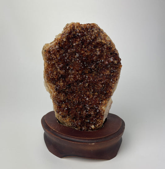 Citrine cluster with deep, orange-colored crystal formations on a wooden stand against a gray background.