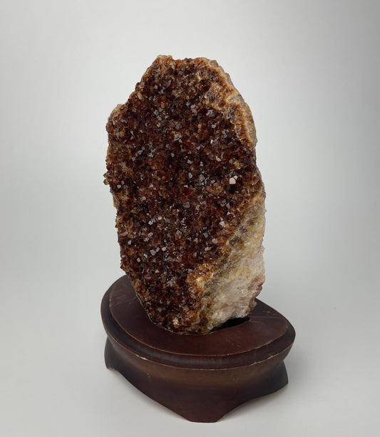 Citrine cluster with deep, orange-colored crystal formations on a wooden stand against a gray background.