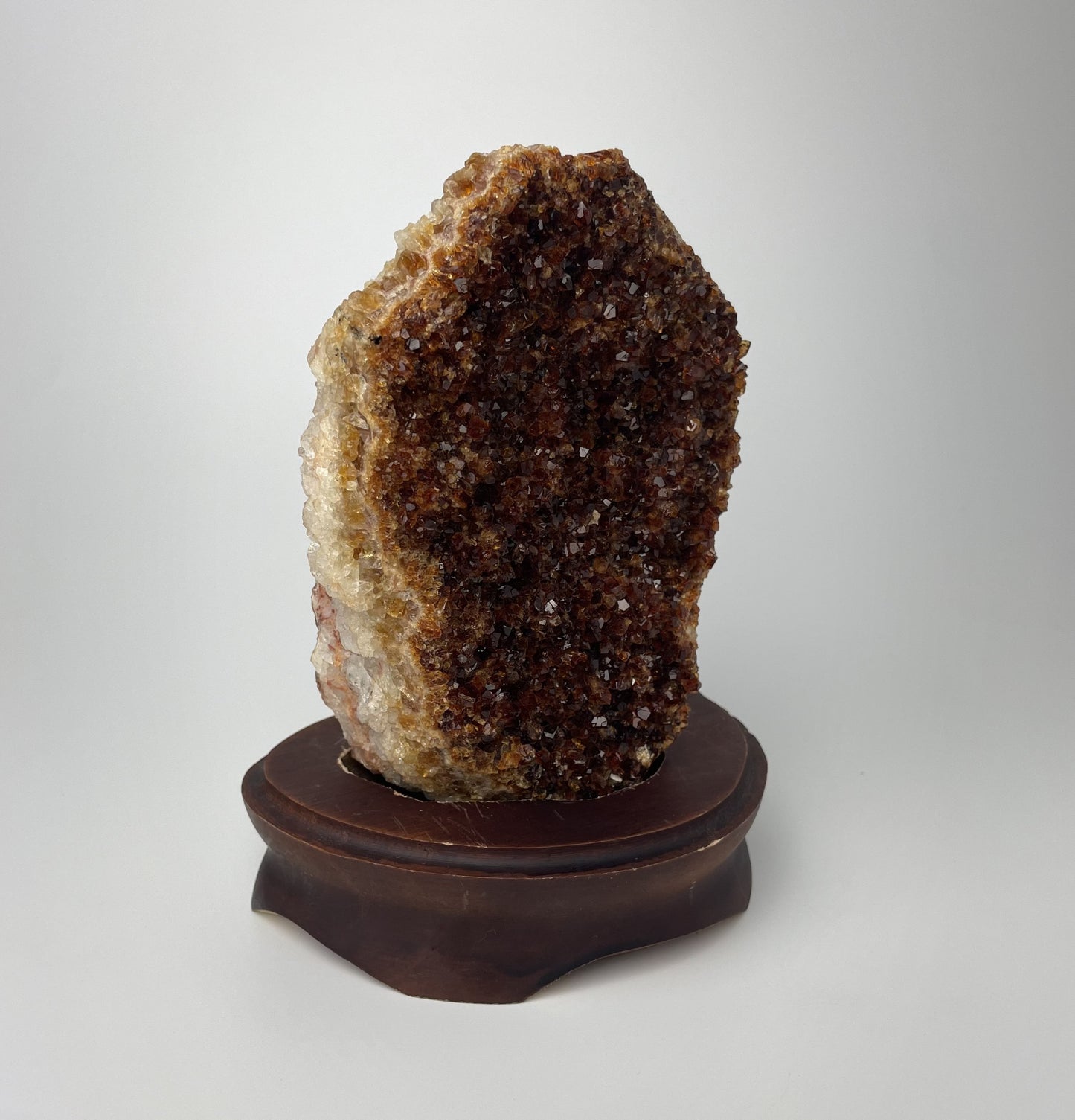 Citrine cluster with deep, orange-colored crystal formations on a wooden stand against a gray background.