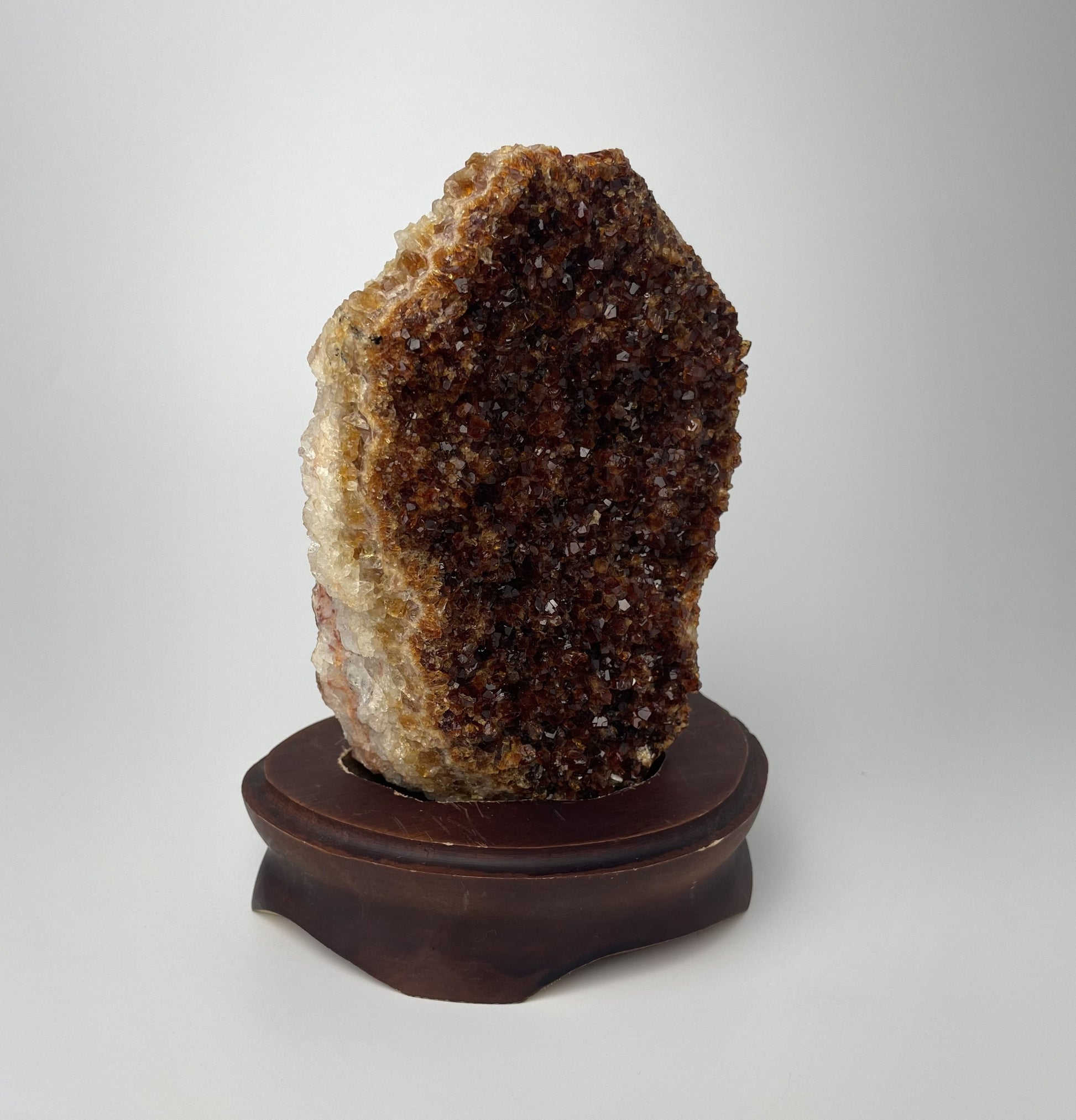 Citrine cluster with deep, orange-colored crystal formations on a wooden stand against a gray background.