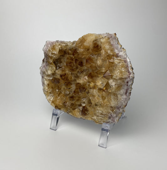 Citrine cluster with deep, orange-colored crystal formations on an acrylic stand against a gray background.