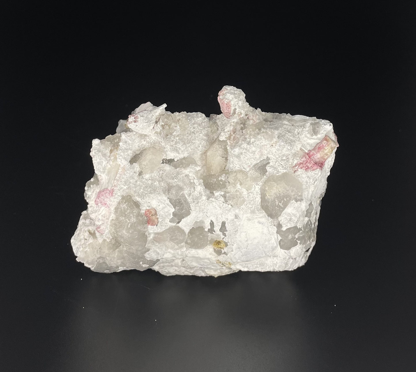 A close-up image of a mineral specimen featuring creamy Orthoclase crystals intergrown with clear quartz and dark tourmaline, showcasing a striking blend of textures and colors.