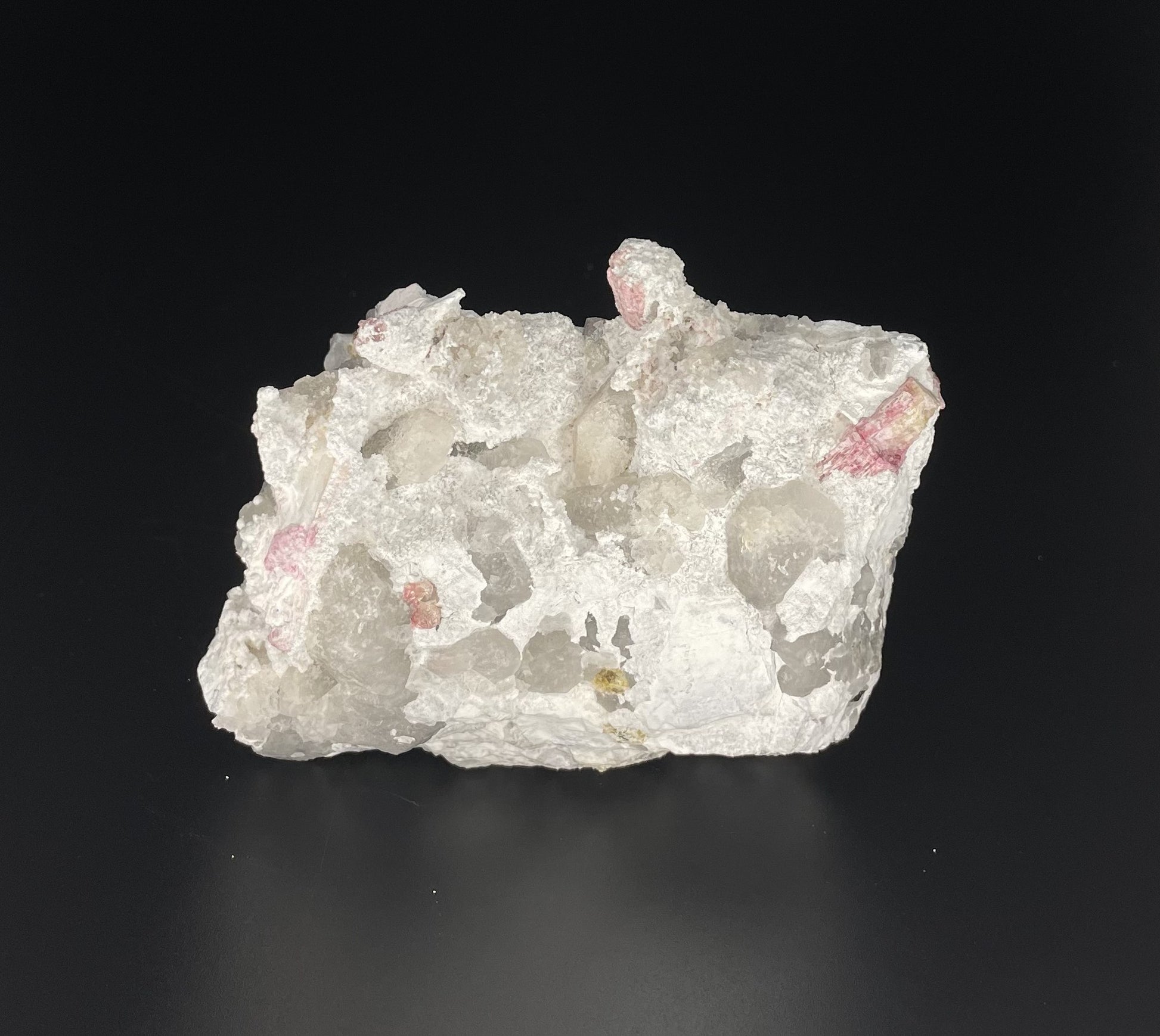 A close-up image of a mineral specimen featuring creamy Orthoclase crystals intergrown with clear quartz and dark tourmaline, showcasing a striking blend of textures and colors.