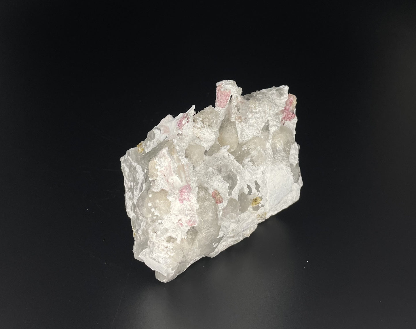 A close-up image of a mineral specimen featuring creamy Orthoclase crystals intergrown with clear quartz and dark tourmaline, showcasing a striking blend of textures and colors.