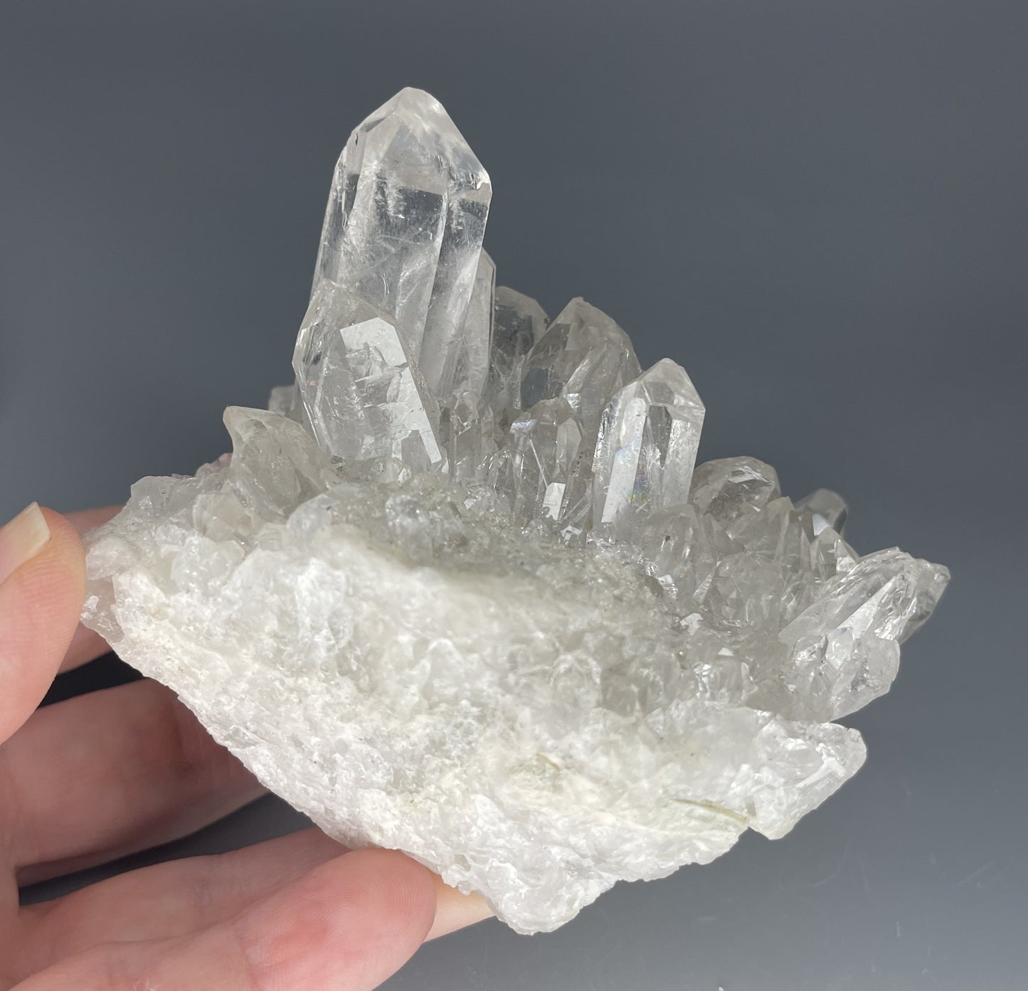 A natural Clear Quartz cluster with multiple crystal points, reflecting light beautifully against a neutral background.
