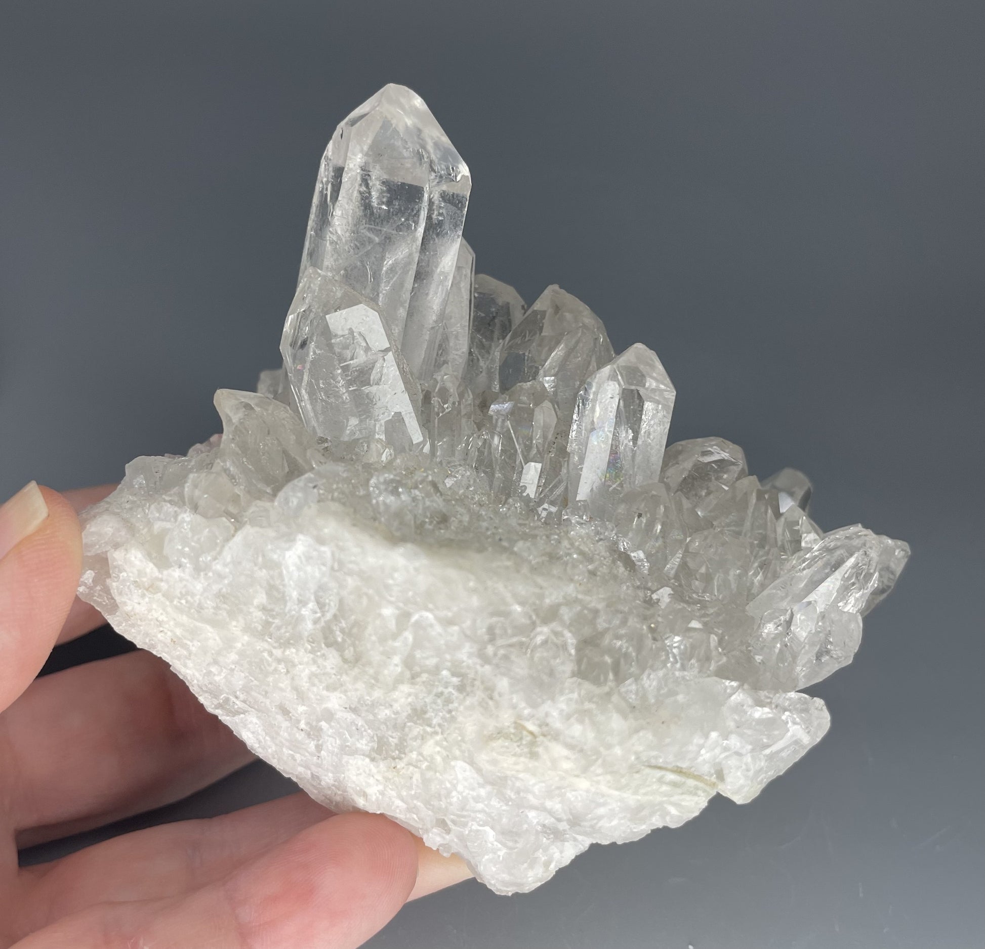 A natural Clear Quartz cluster with multiple crystal points, reflecting light beautifully against a neutral background.