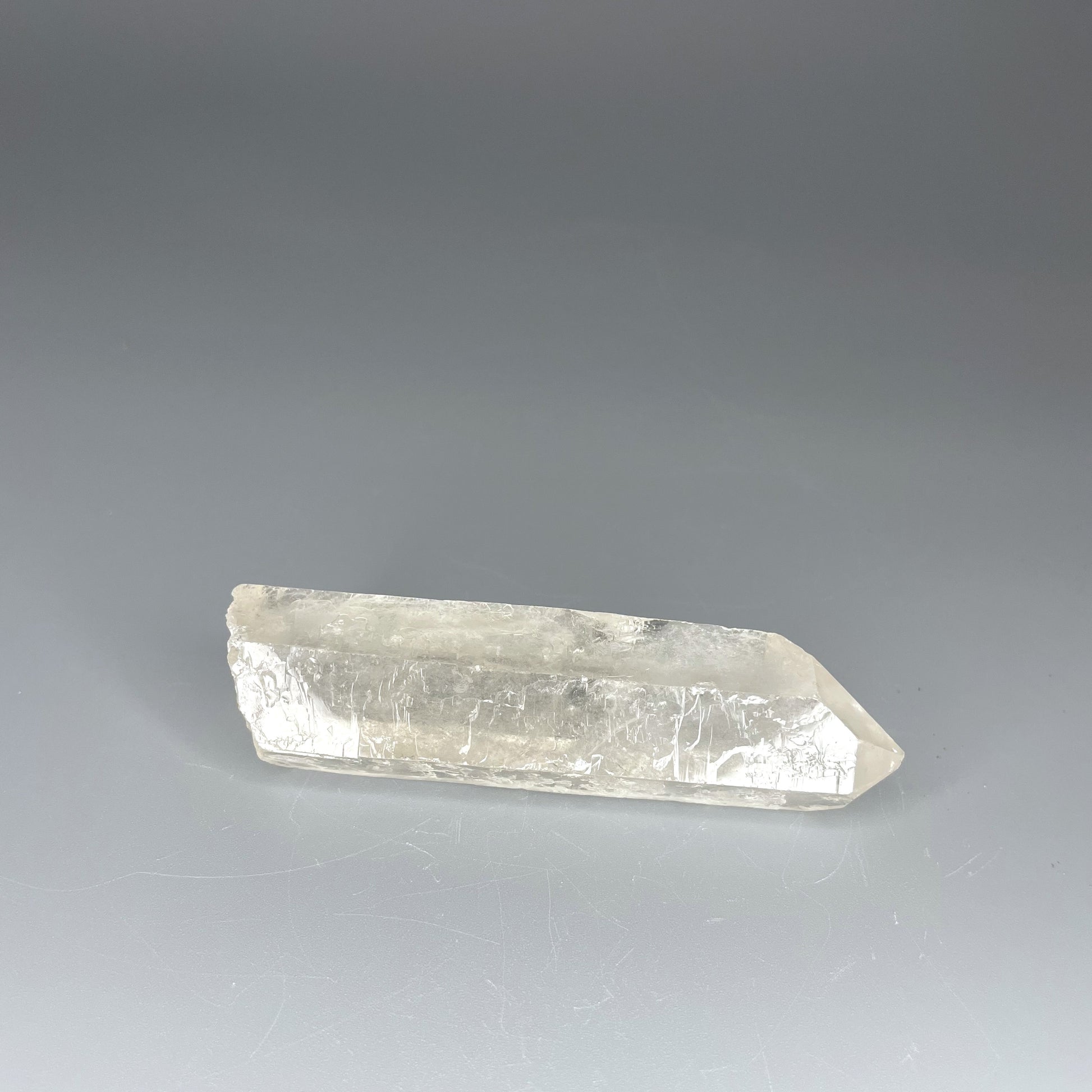 A 4-inch polished Clear Quartz point with a smooth finish, standing upright against a neutral background.