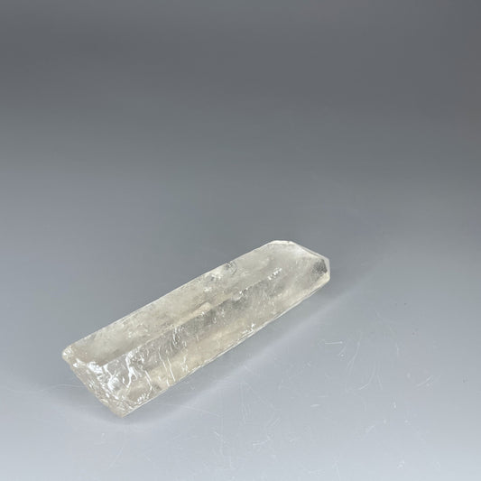A 4-inch polished Clear Quartz point with a smooth finish, standing upright against a neutral background.