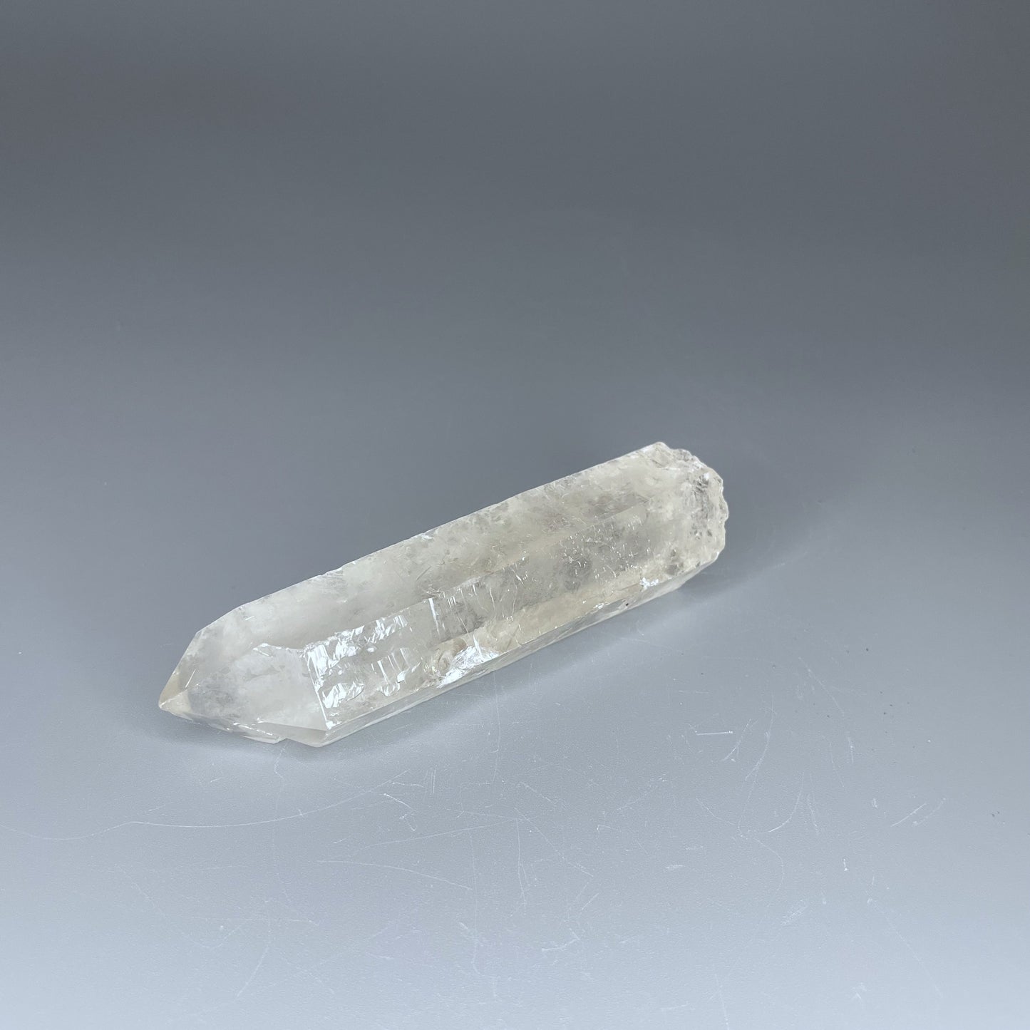 A 4-inch polished Clear Quartz point with a smooth finish, standing upright against a neutral background.