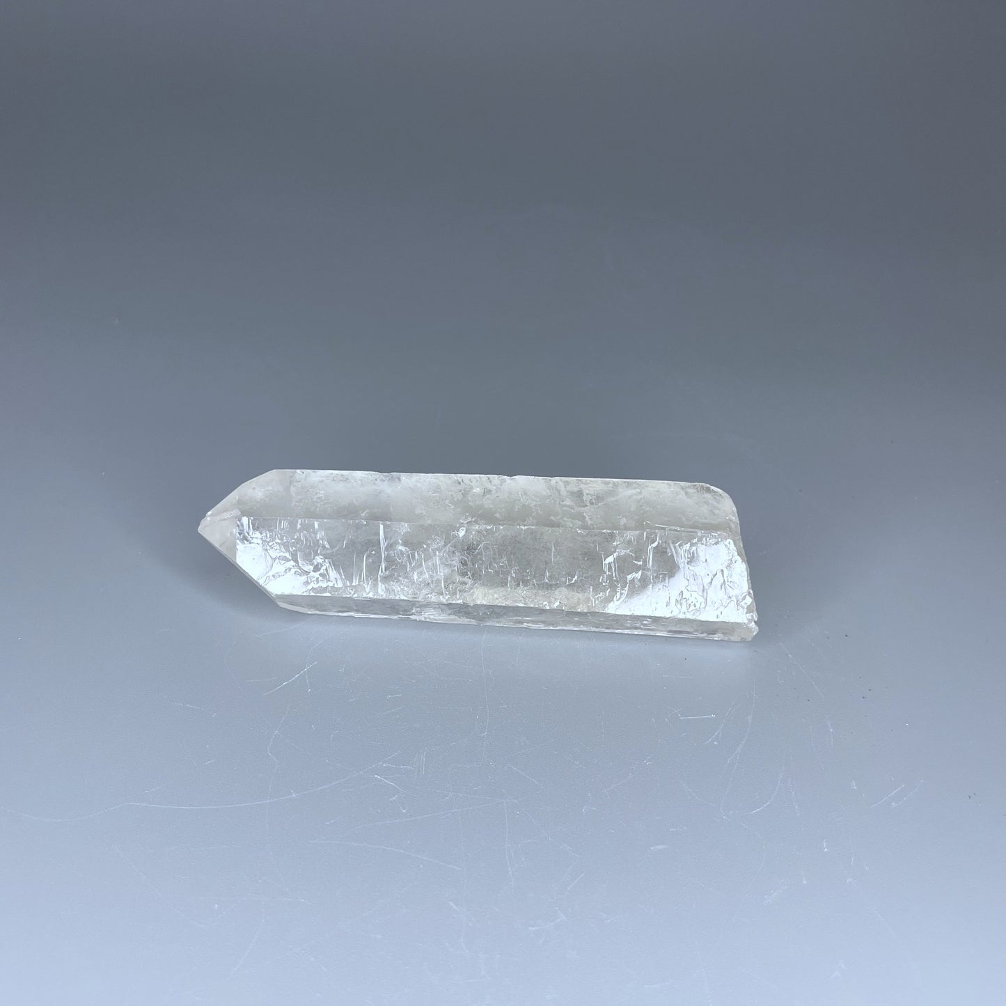 A 4-inch polished Clear Quartz point with a smooth finish, standing upright against a neutral background.
