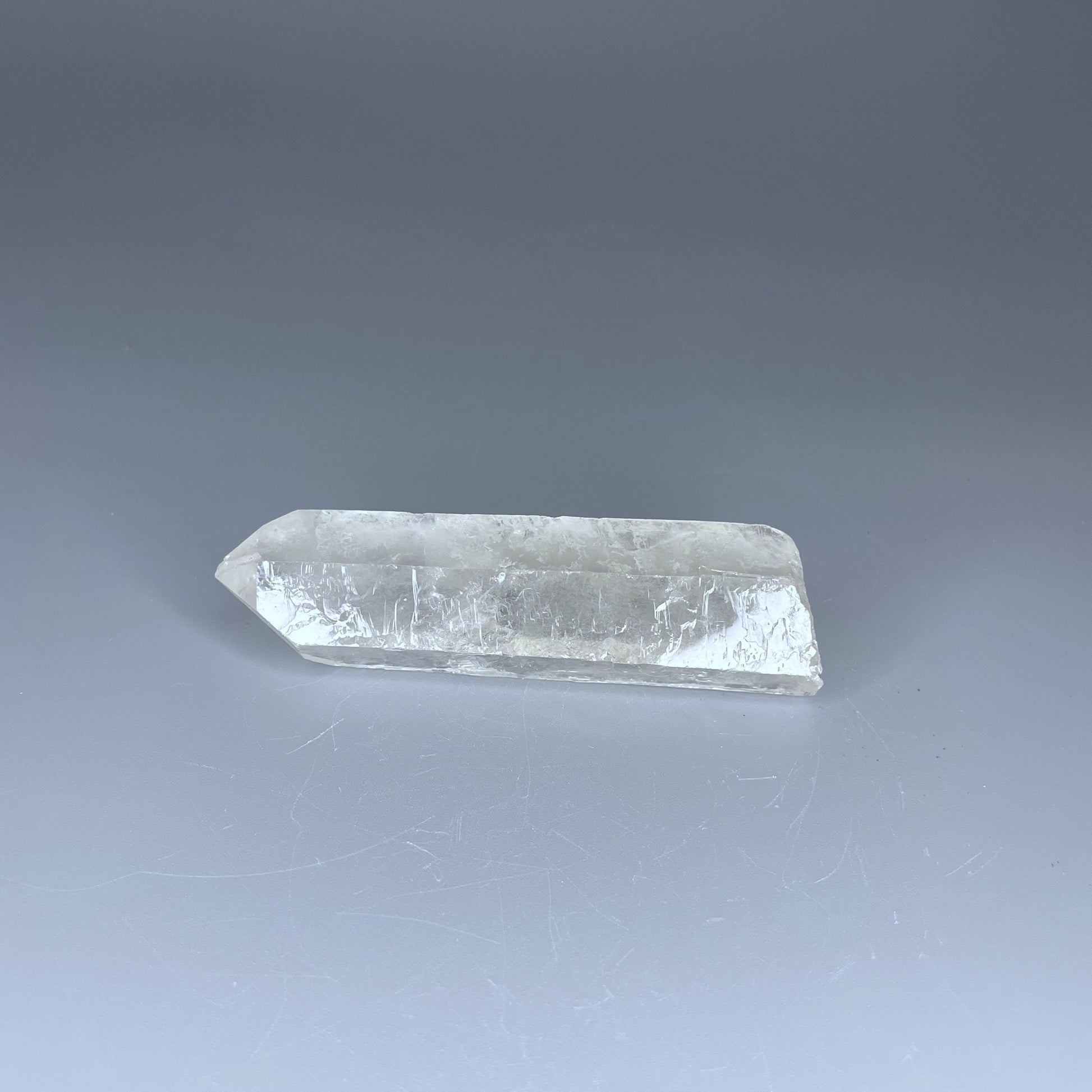 A 4-inch polished Clear Quartz point with a smooth finish, standing upright against a neutral background.
