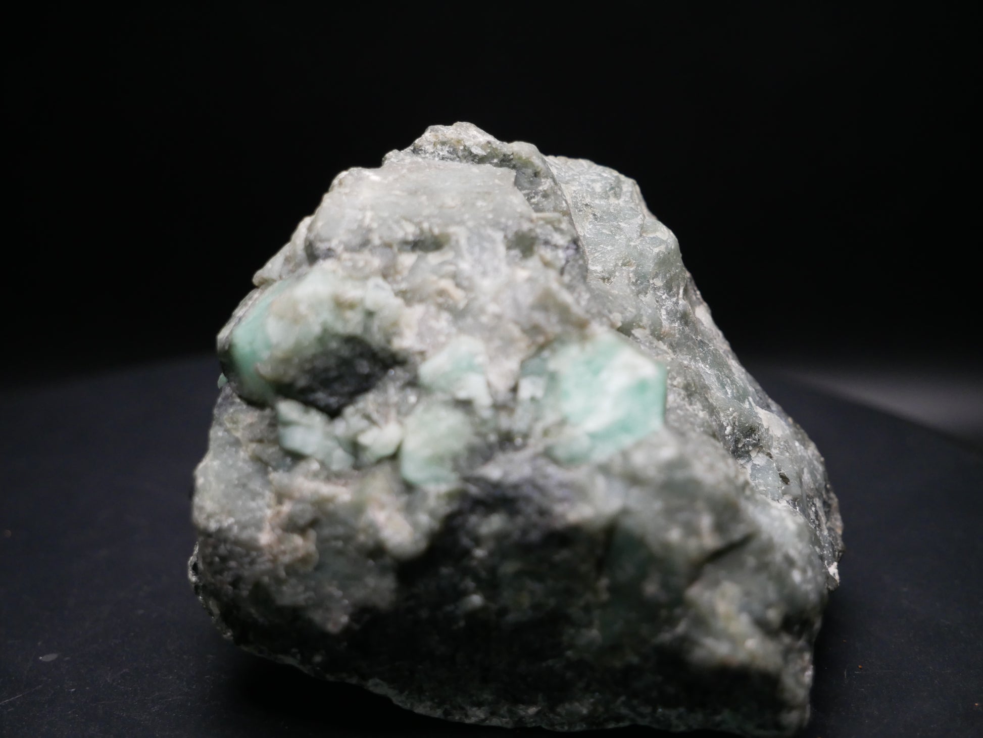 A large emerald in a matrix with distinctive emeralds protruding from the matrix on a black background.