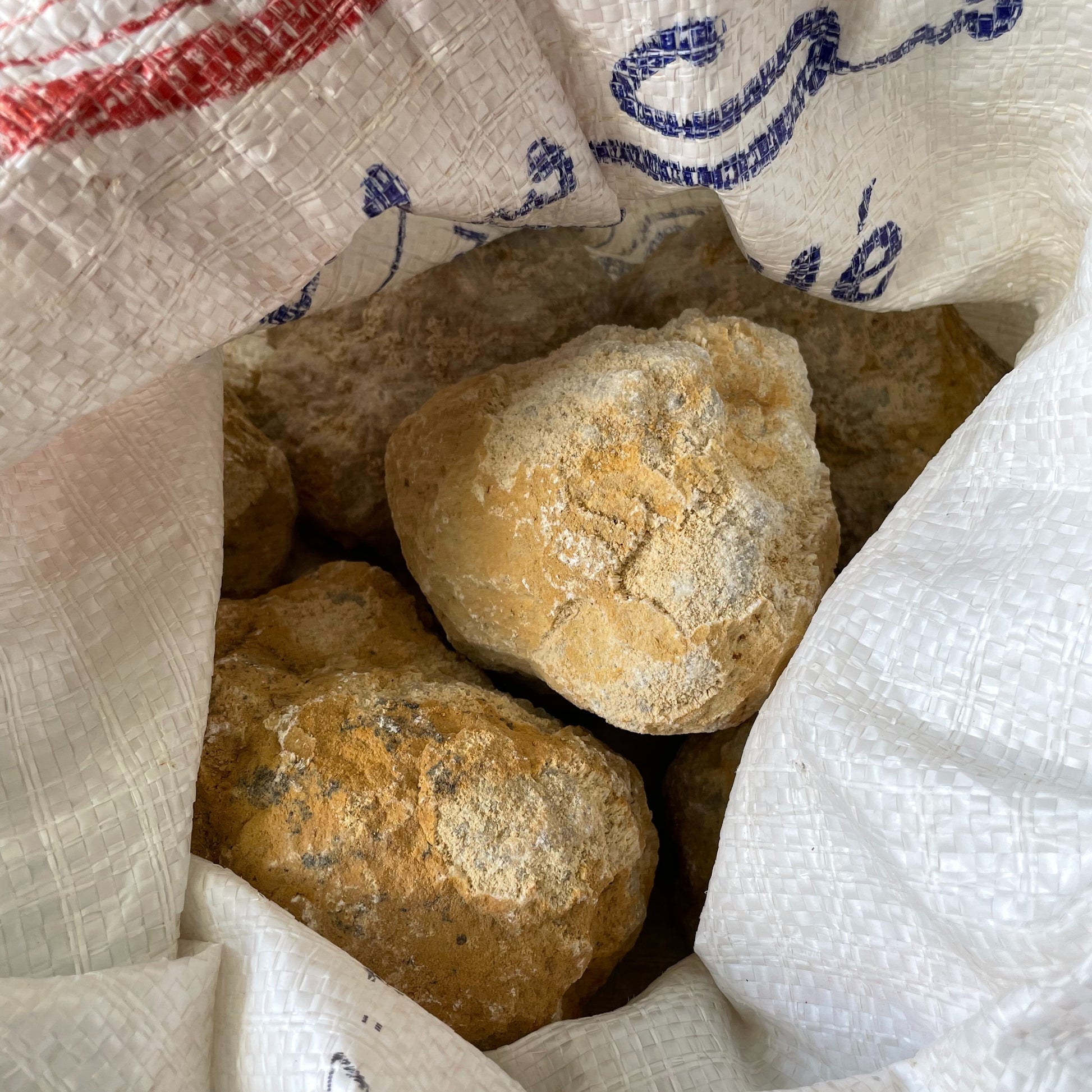 A large break-your-own geode resting on a wooden surface, displaying a rugged exterior with visible cracks hinting at the sparkling crystals hidden within.