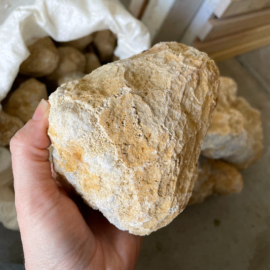 A large break-your-own geode resting on a wooden surface, displaying a rugged exterior with visible cracks hinting at the sparkling crystals hidden within.