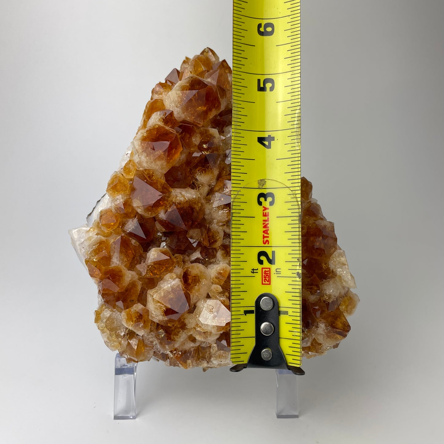 Citrine cluster with deep, orange-colored crystal formations on an acrylic stand against a gray background.