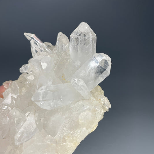 A natural Clear Quartz cluster with multiple crystal points, reflecting light beautifully against a neutral background.
