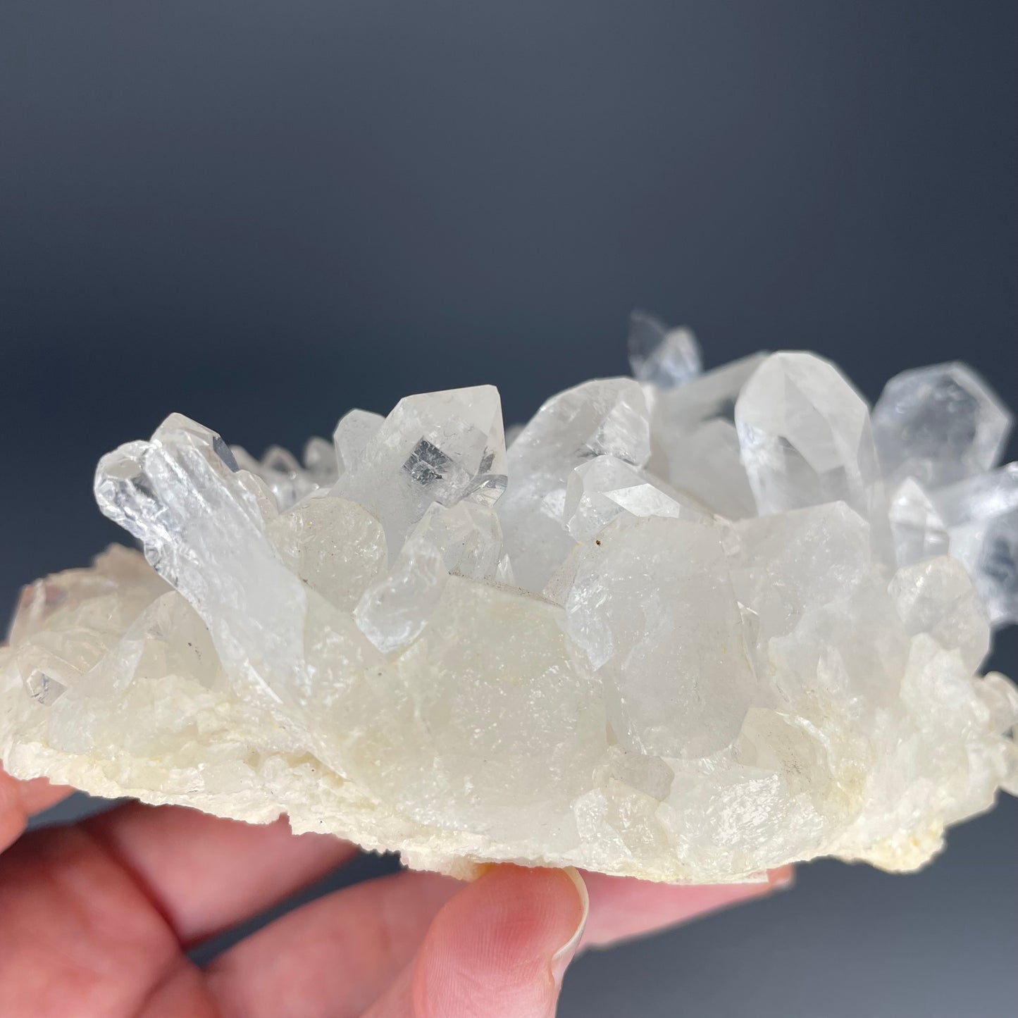 A natural Clear Quartz cluster with multiple crystal points, reflecting light beautifully against a neutral background.