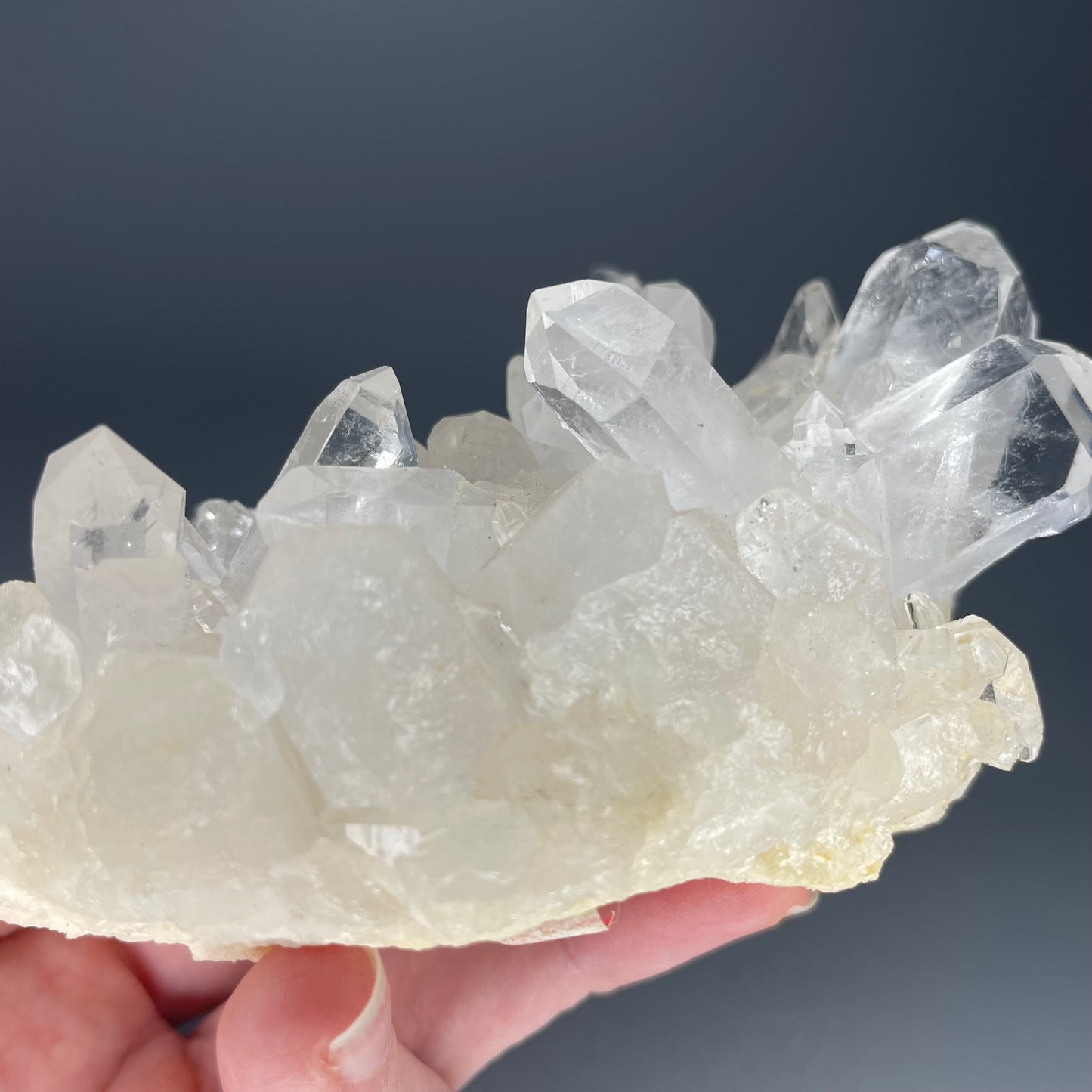 A natural Clear Quartz cluster with multiple crystal points, reflecting light beautifully against a neutral background.