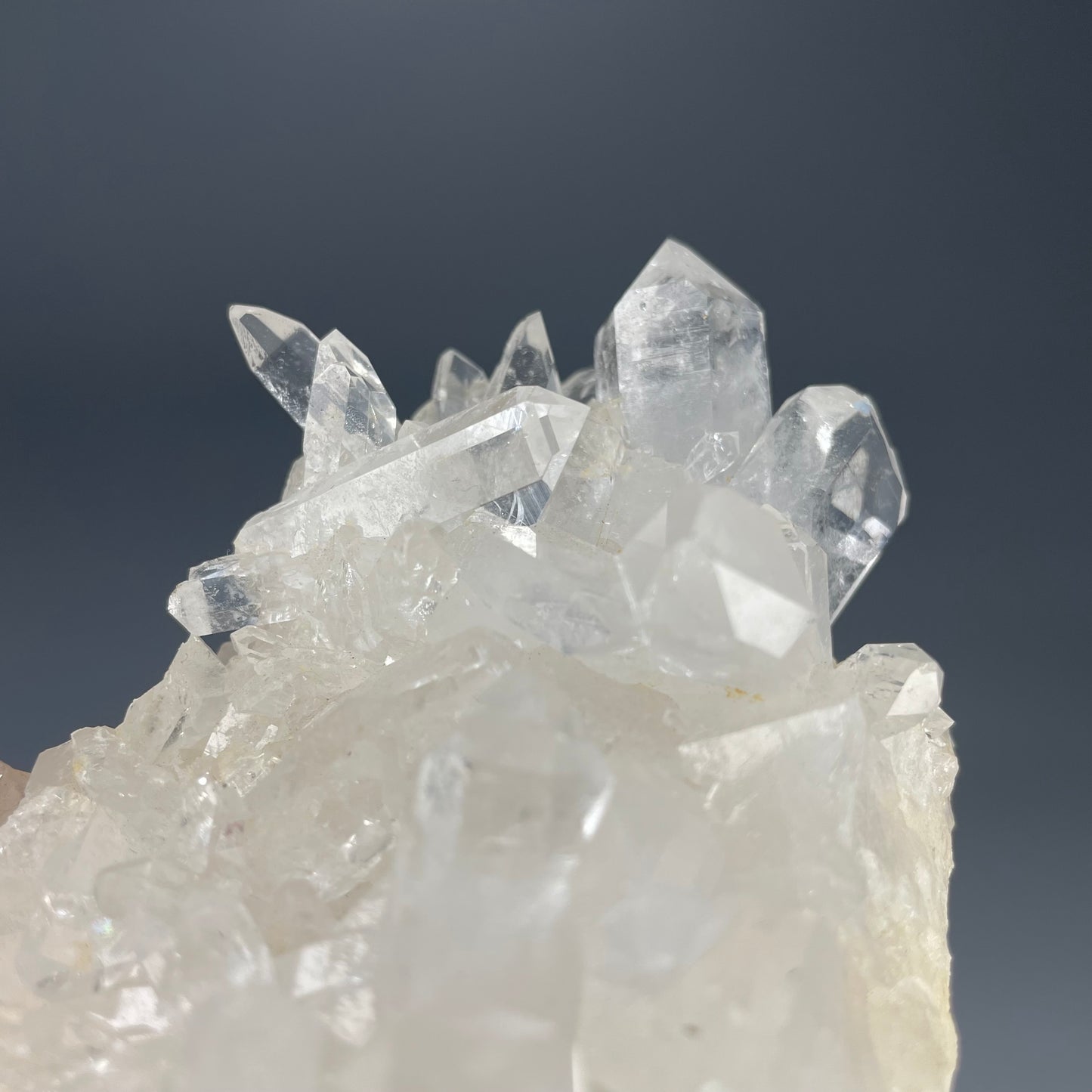 A natural Clear Quartz cluster with multiple crystal points, reflecting light beautifully against a neutral background.