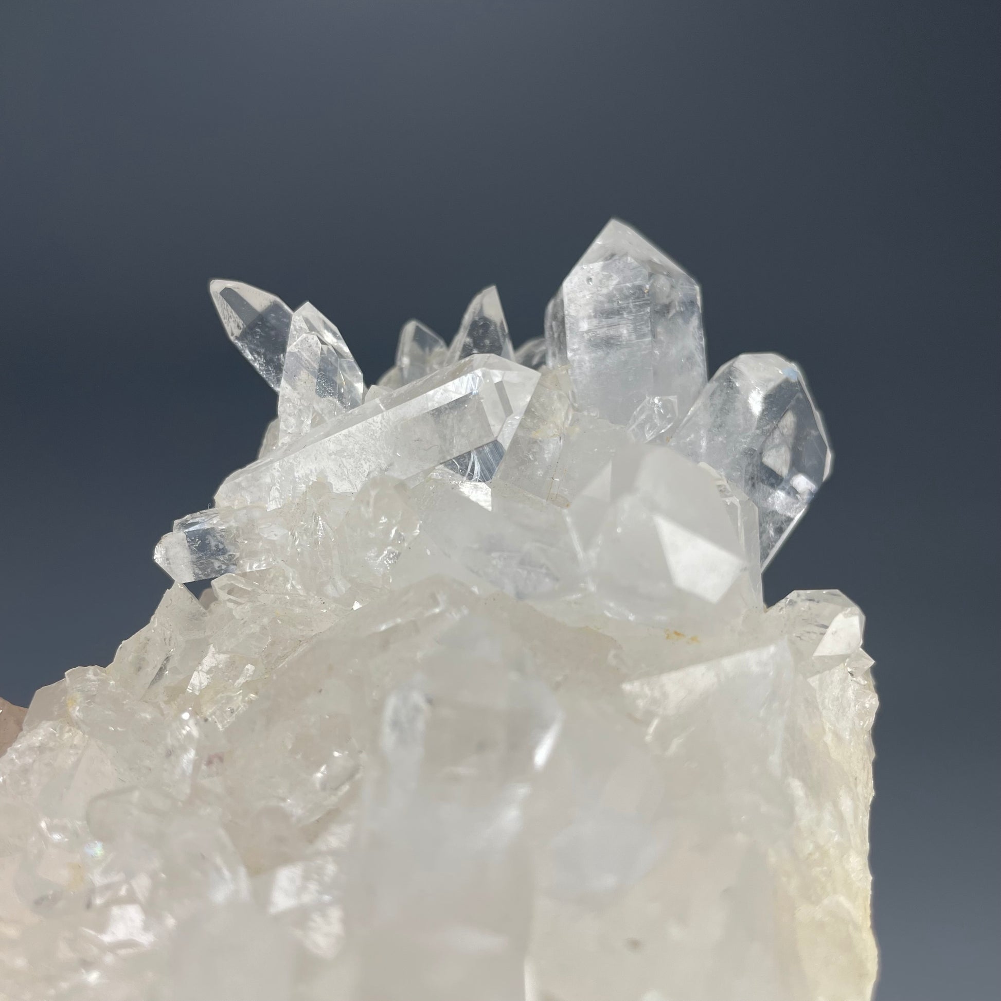 A natural Clear Quartz cluster with multiple crystal points, reflecting light beautifully against a neutral background.