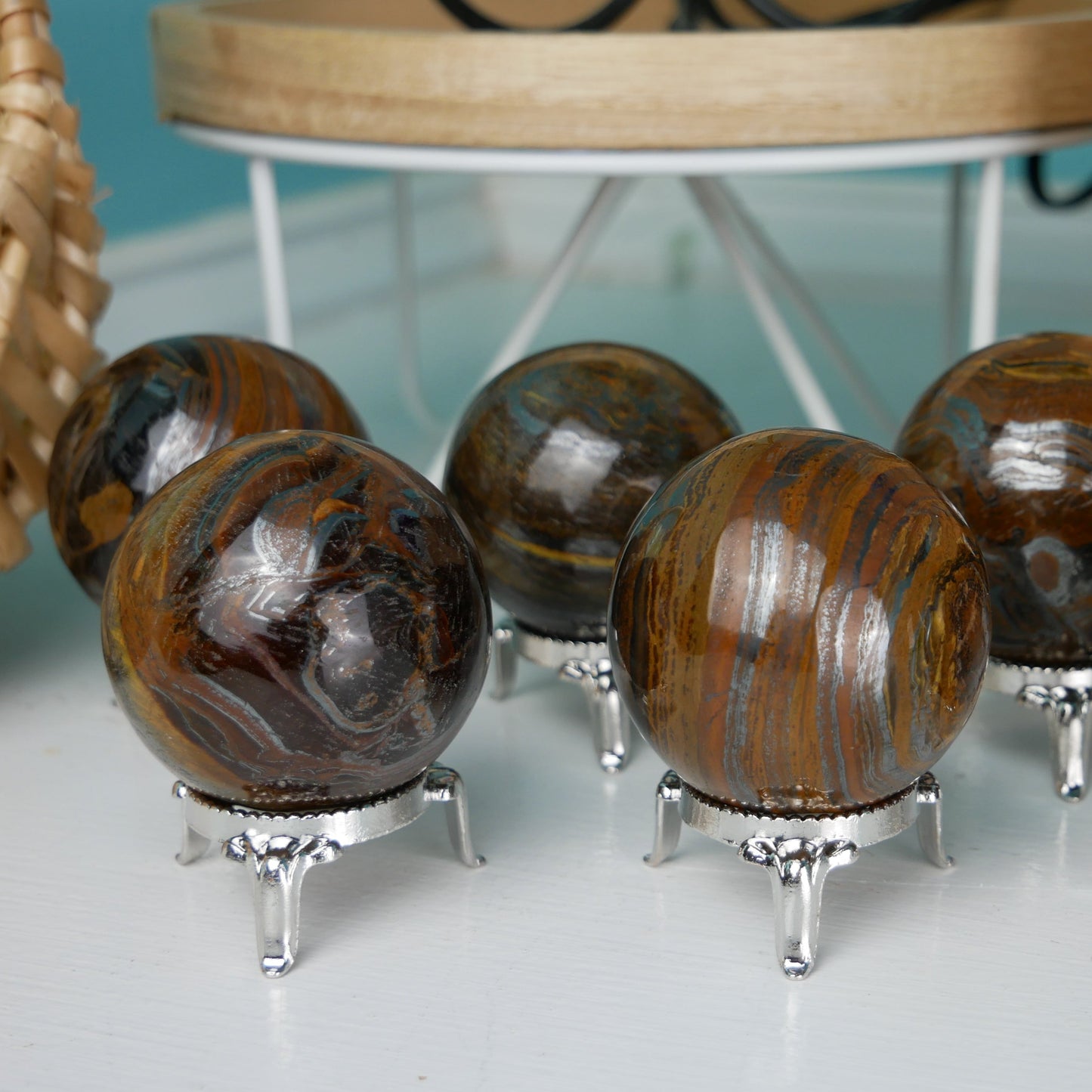 A Tiger Iron Sphere, measuring 2 inches in diameter, sits on a wooden display stand. The sphere exhibits a mesmerizing blend of golden, rusty red, and deep brown hues, reminiscent of a tiger's stripes. Its polished surface reflects light, revealing intricate patterns and textures within the natural layers of the stone.