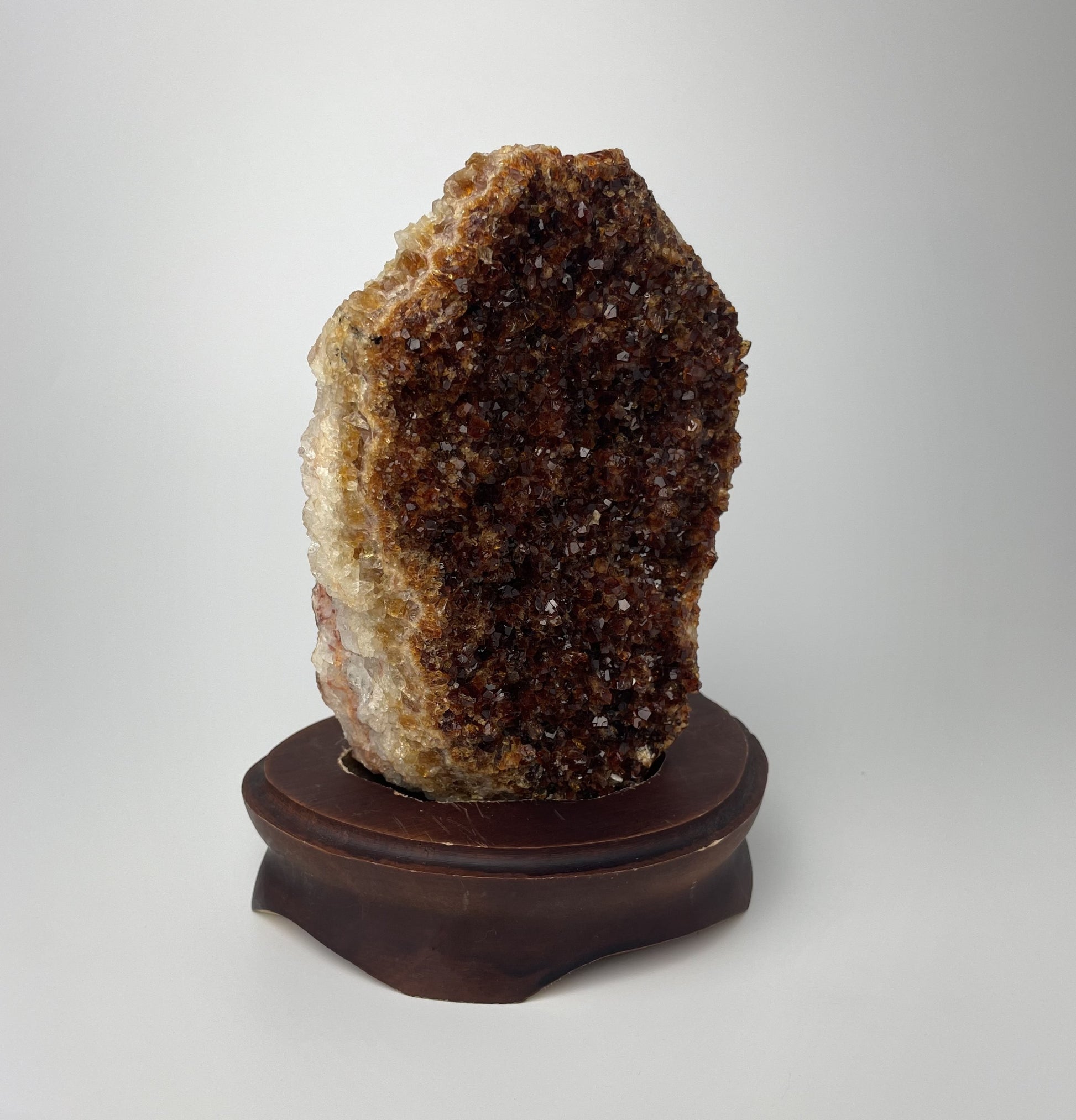 Citrine cluster with deep, orange-colored crystal formations on a wooden stand against a gray background. 