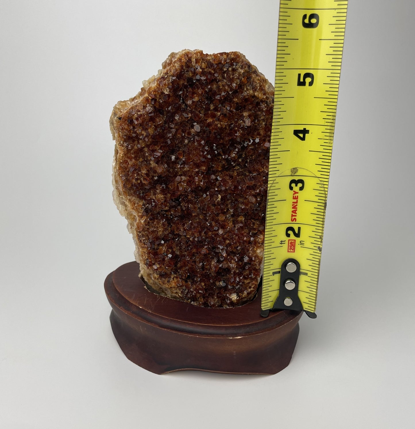 Citrine cluster with deep, orange-colored crystal formations on a wooden stand against a gray background. 