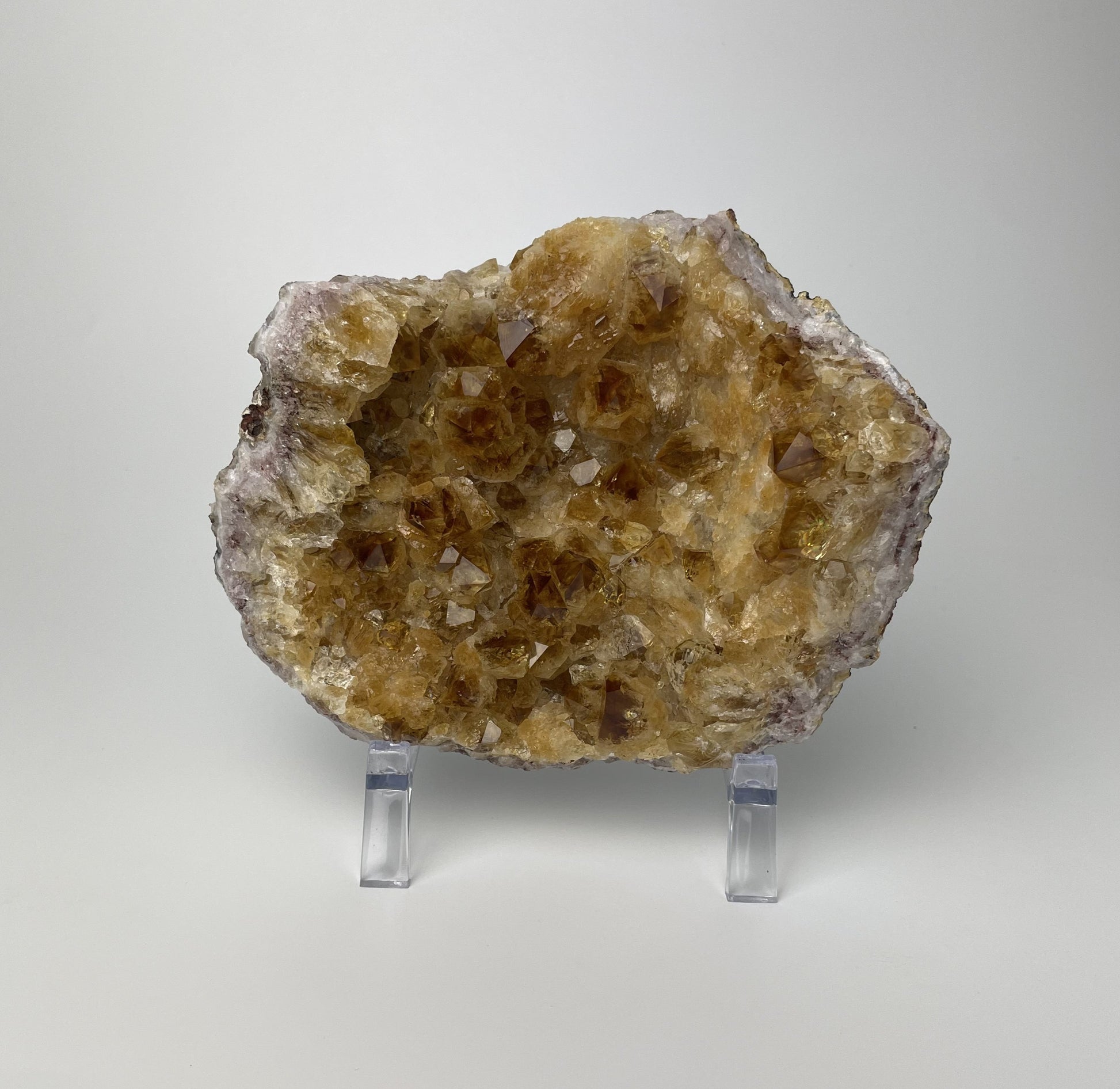 Citrine cluster with deep, orange-colored crystal formations on an acrylic stand against a gray background. 