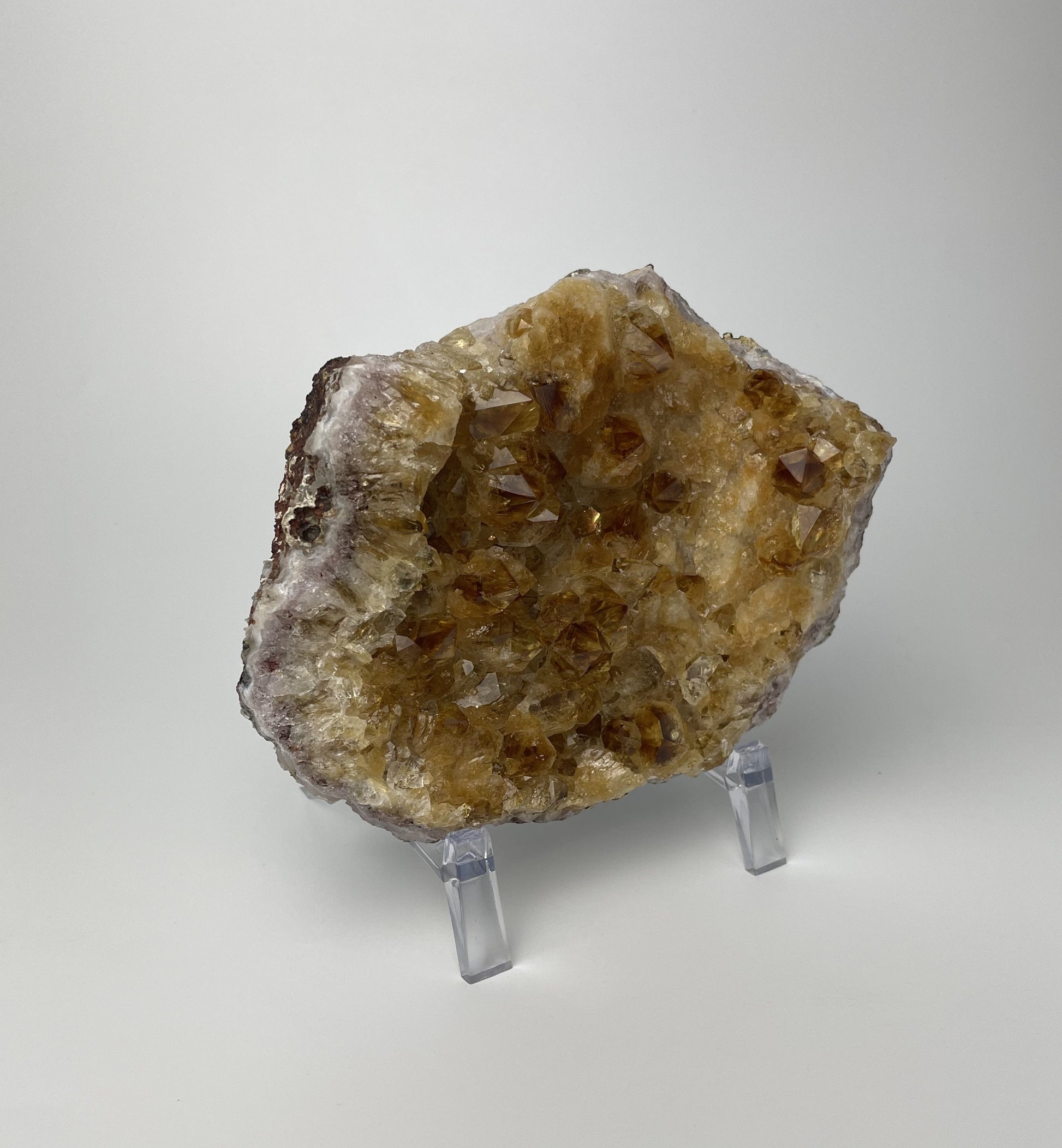 Citrine cluster with deep, orange-colored crystal formations on an acrylic stand against a gray background. 