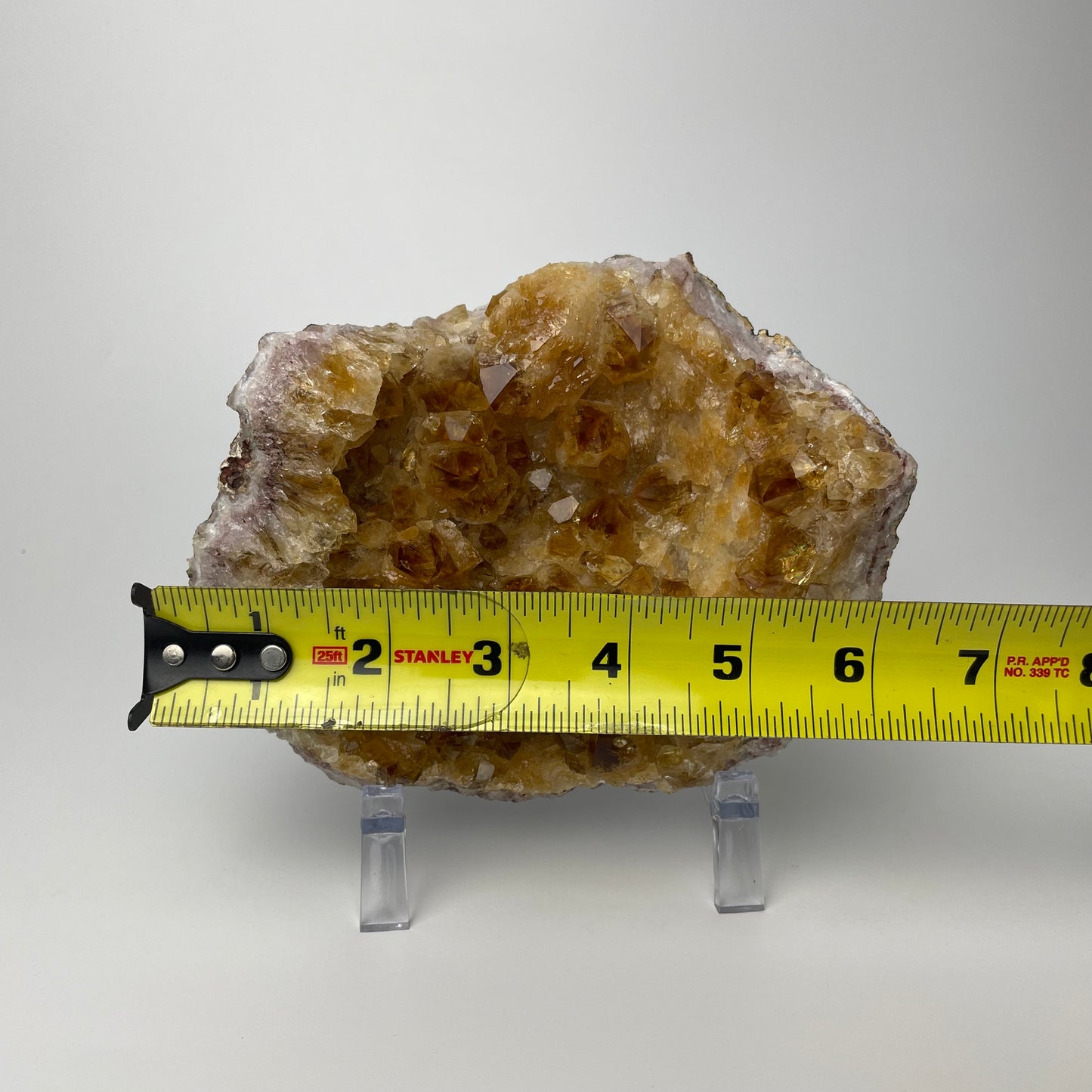 Citrine cluster with deep, orange-colored crystal formations on an acrylic stand against a gray background. 