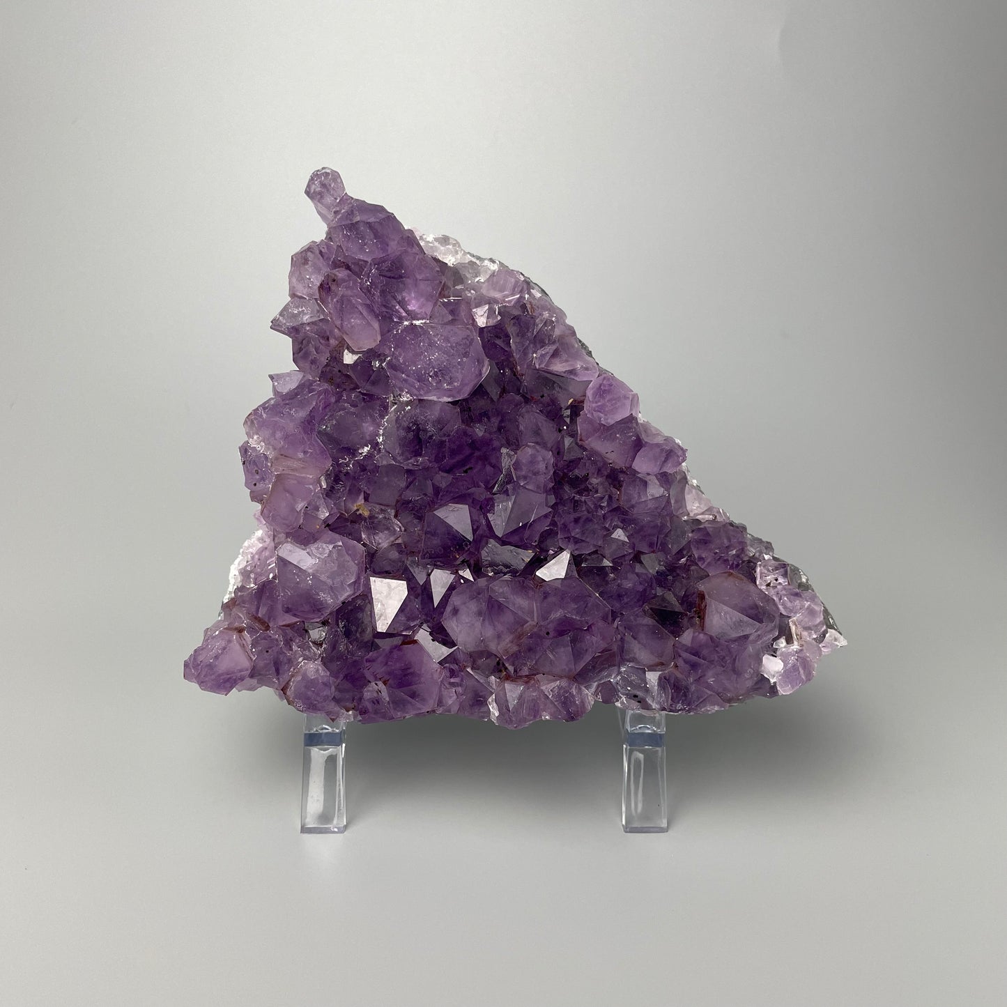 Amethyst cluster with brilliant hues of purple and various sizes of crystal formations on a gray background.