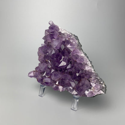 Amethyst cluster with brilliant hues of purple and various sizes of crystal formations on a gray background.