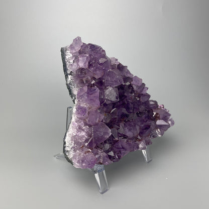 Amethyst cluster with brilliant hues of purple and various sizes of crystal formations on a gray background.