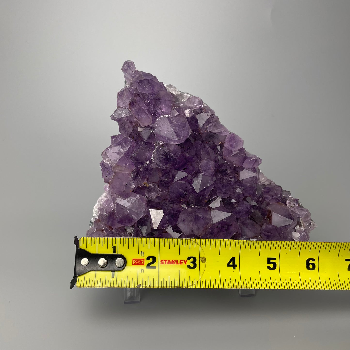 Amethyst cluster with brilliant hues of purple and various sizes of crystal formations on a gray background.