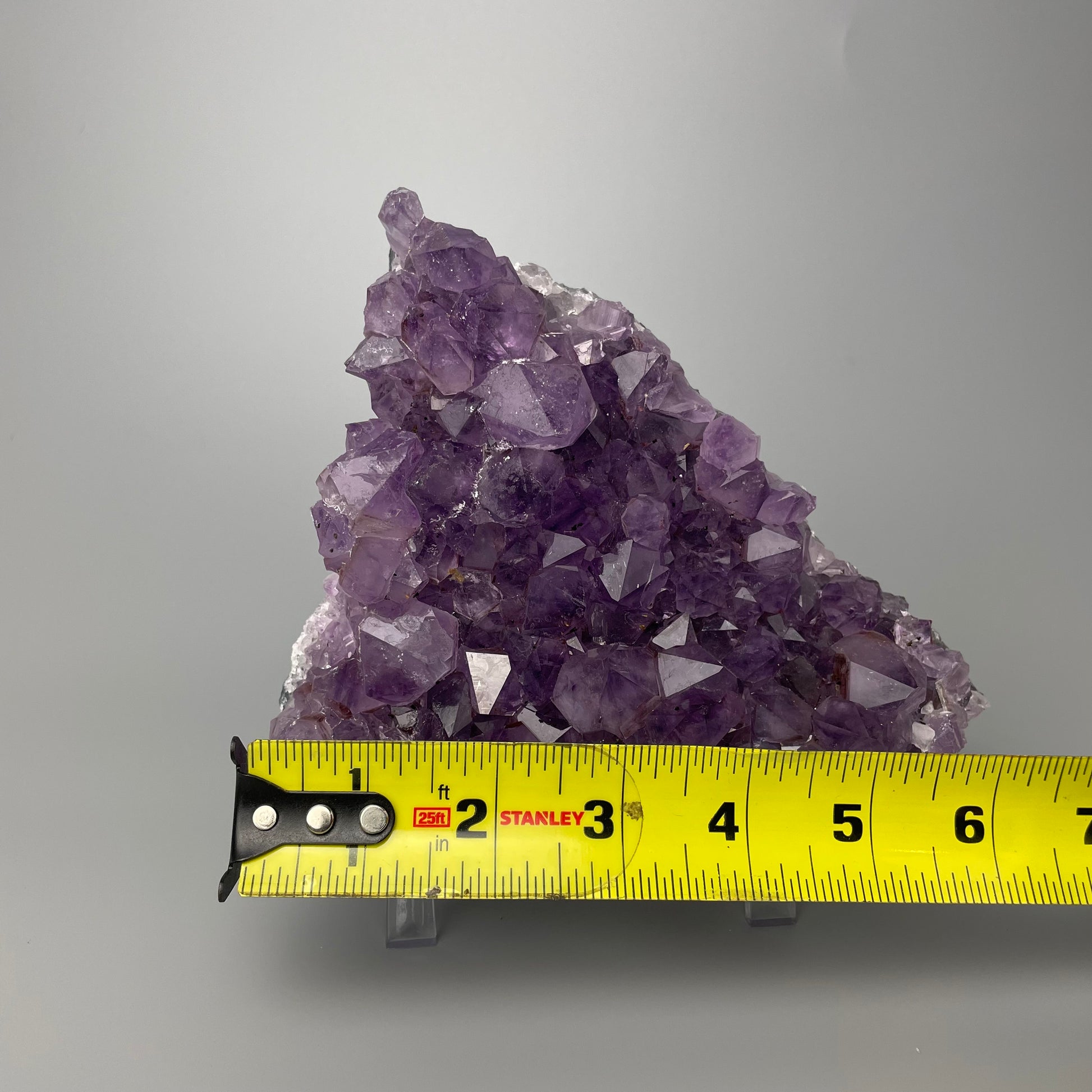 Amethyst cluster with brilliant hues of purple and various sizes of crystal formations on a gray background.