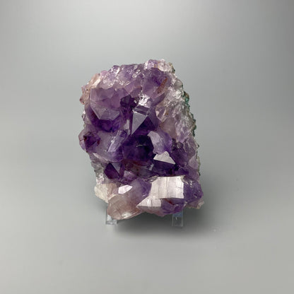 Amethyst cluster with brilliant hues of purple and various sizes of crystal formations on a gray background.