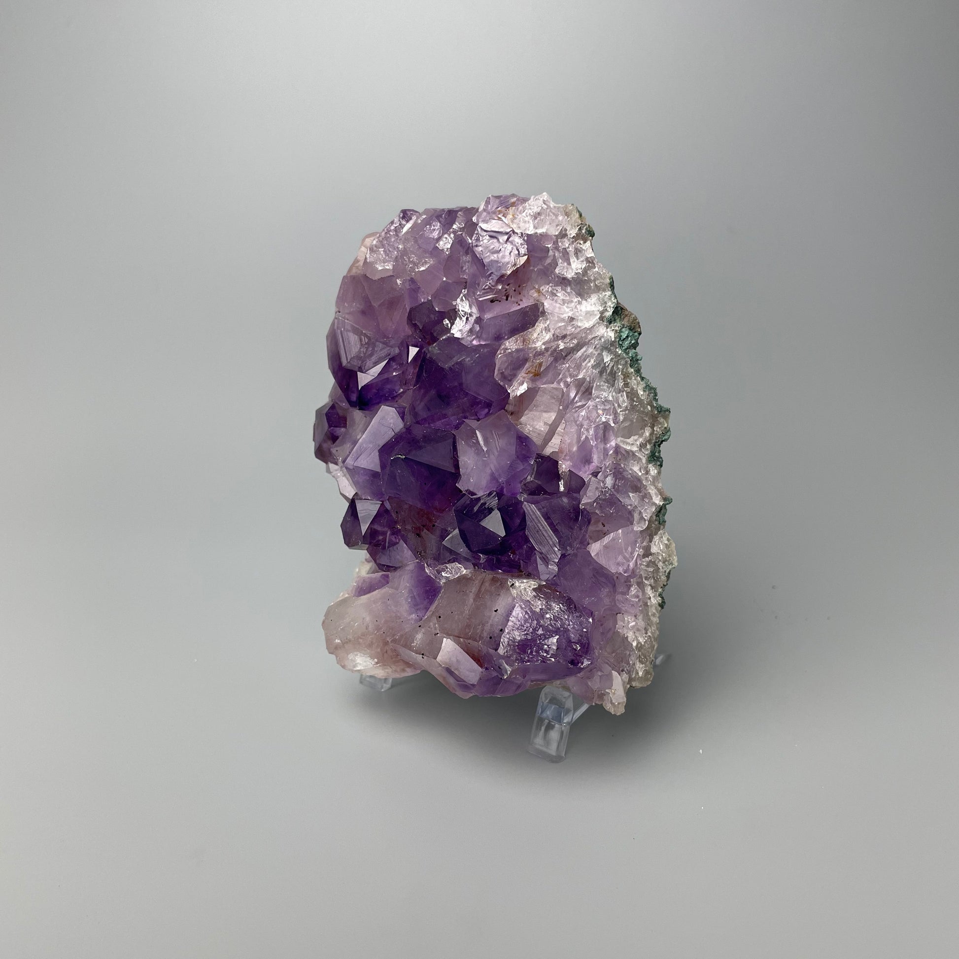 Amethyst cluster with brilliant hues of purple and various sizes of crystal formations on a gray background.