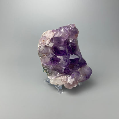 Amethyst cluster with brilliant hues of purple and various sizes of crystal formations on a gray background.