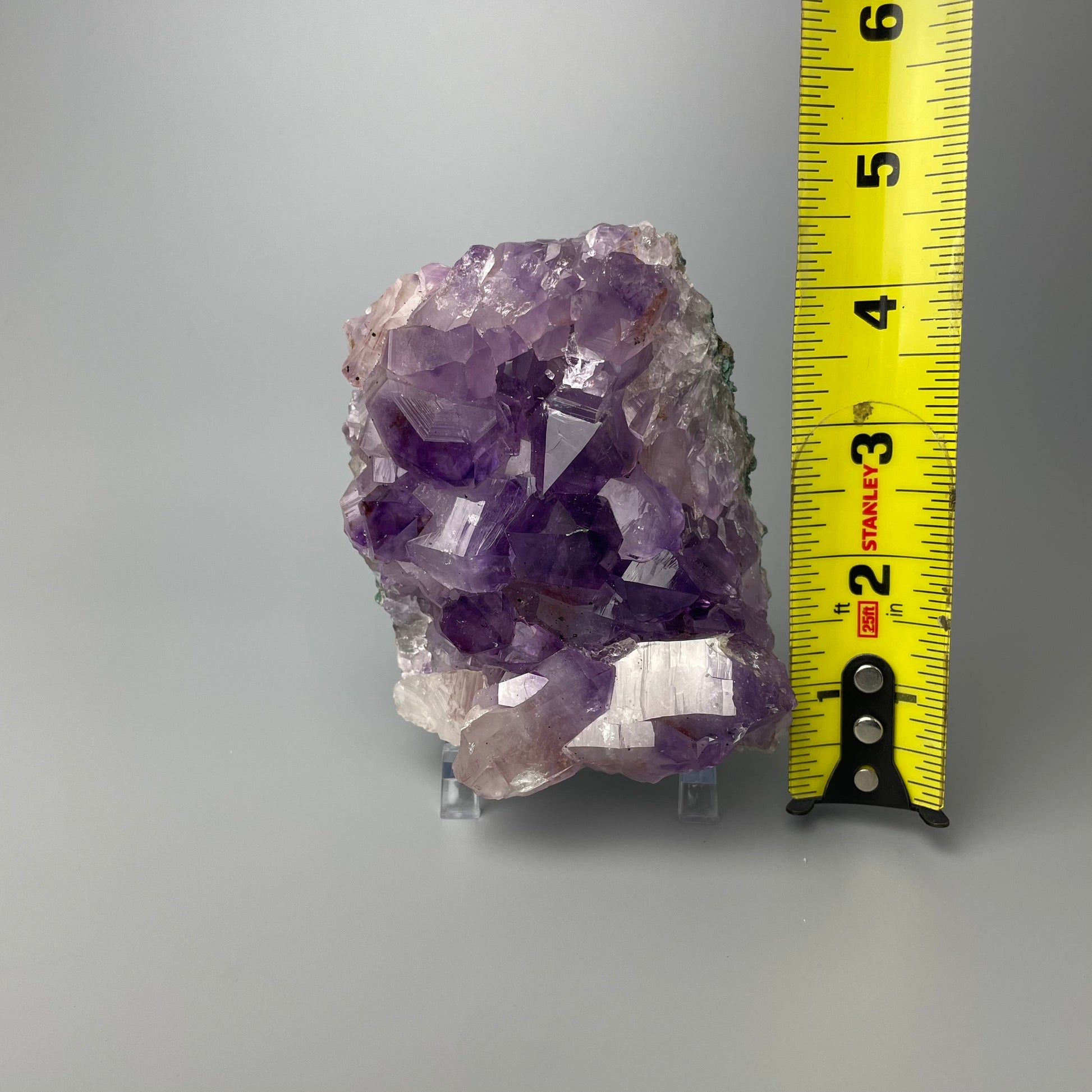 Amethyst cluster with brilliant hues of purple and various sizes of crystal formations on a gray background.