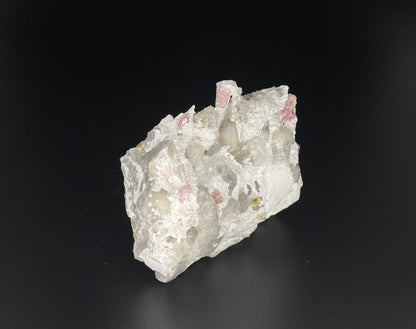  A close-up image of a mineral specimen featuring creamy Orthoclase crystals intergrown with clear quartz and dark tourmaline, showcasing a striking blend of textures and colors.