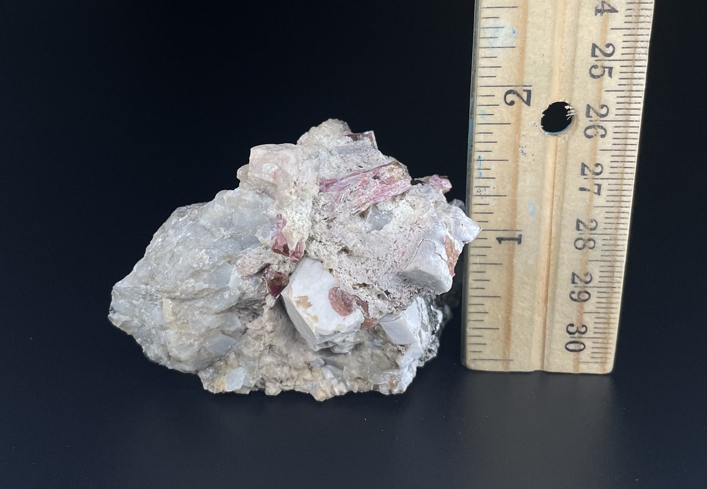 A close-up image of a mineral specimen featuring creamy Orthoclase crystals intergrown with clear quartz and dark tourmaline, showcasing a striking blend of textures and colors