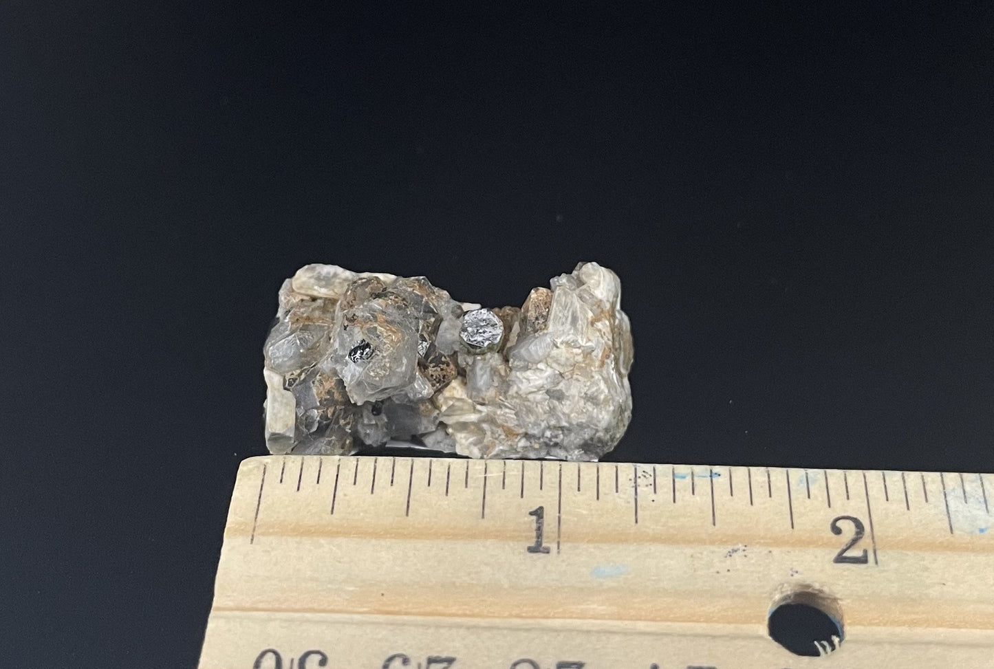 A close-up image of a mineral specimen featuring creamy Orthoclase crystals intergrown with clear quartz and dark tourmaline, showcasing a striking blend of textures and colors