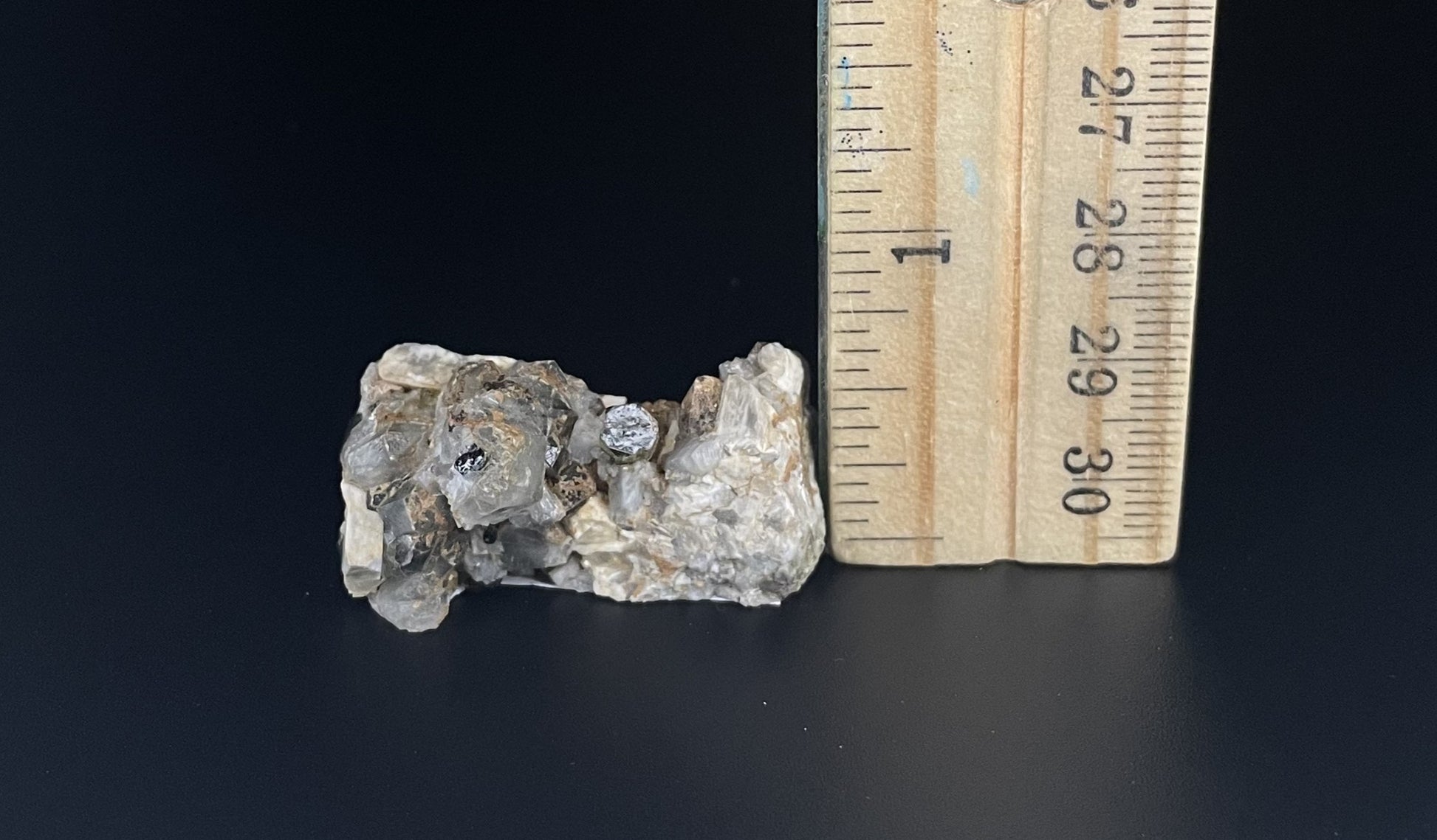 A close-up image of a mineral specimen featuring creamy Orthoclase crystals intergrown with clear quartz and dark tourmaline, showcasing a striking blend of textures and colors