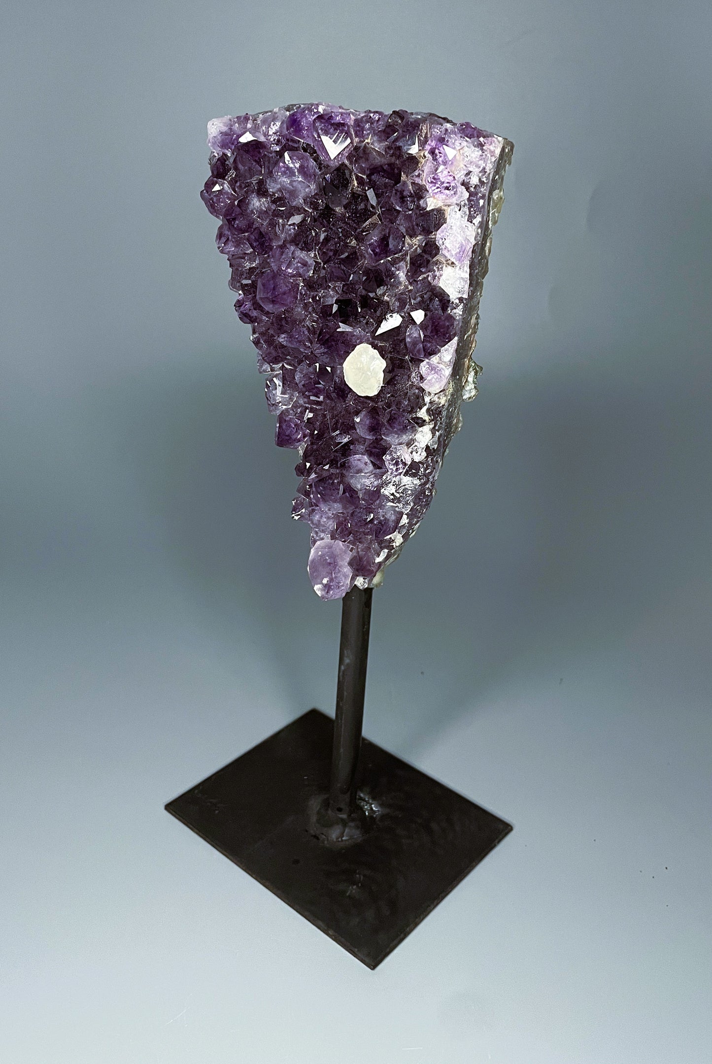 A Brazilian amethyst cluster in a triangular shape with large crystals and calcite growth on a black metal stand.