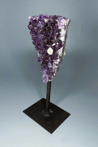 A Brazilian amethyst cluster in a triangular shape with large crystals and calcite growth on a black metal stand.