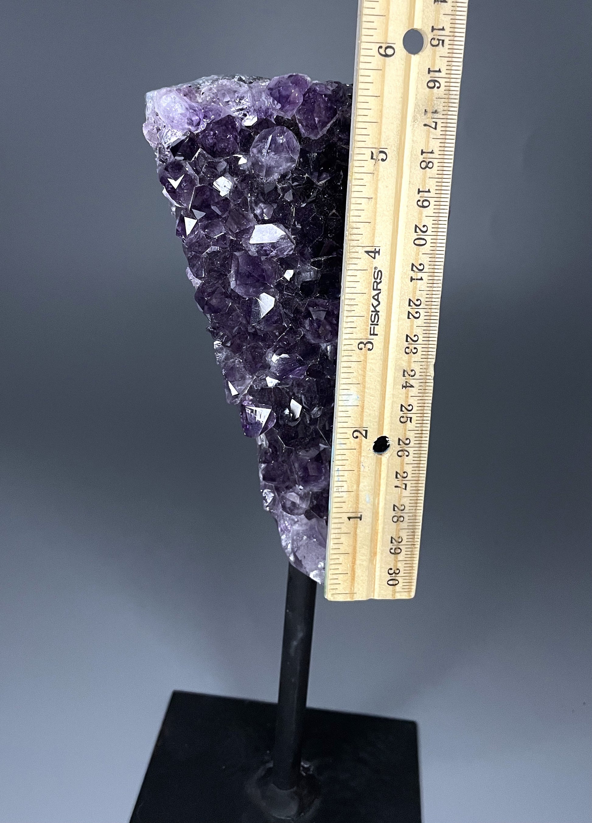 A Brazilian amethyst cluster in a triangular shape with large crystals and calcite growth on a black metal stand.