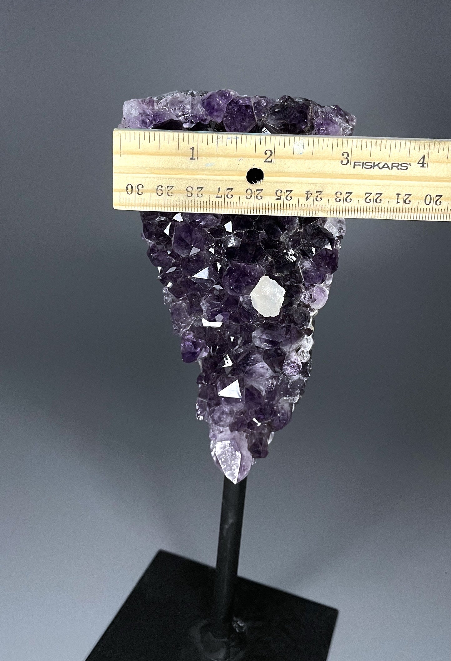 A Brazilian amethyst cluster in a triangular shape with large crystals and calcite growth on a black metal stand.