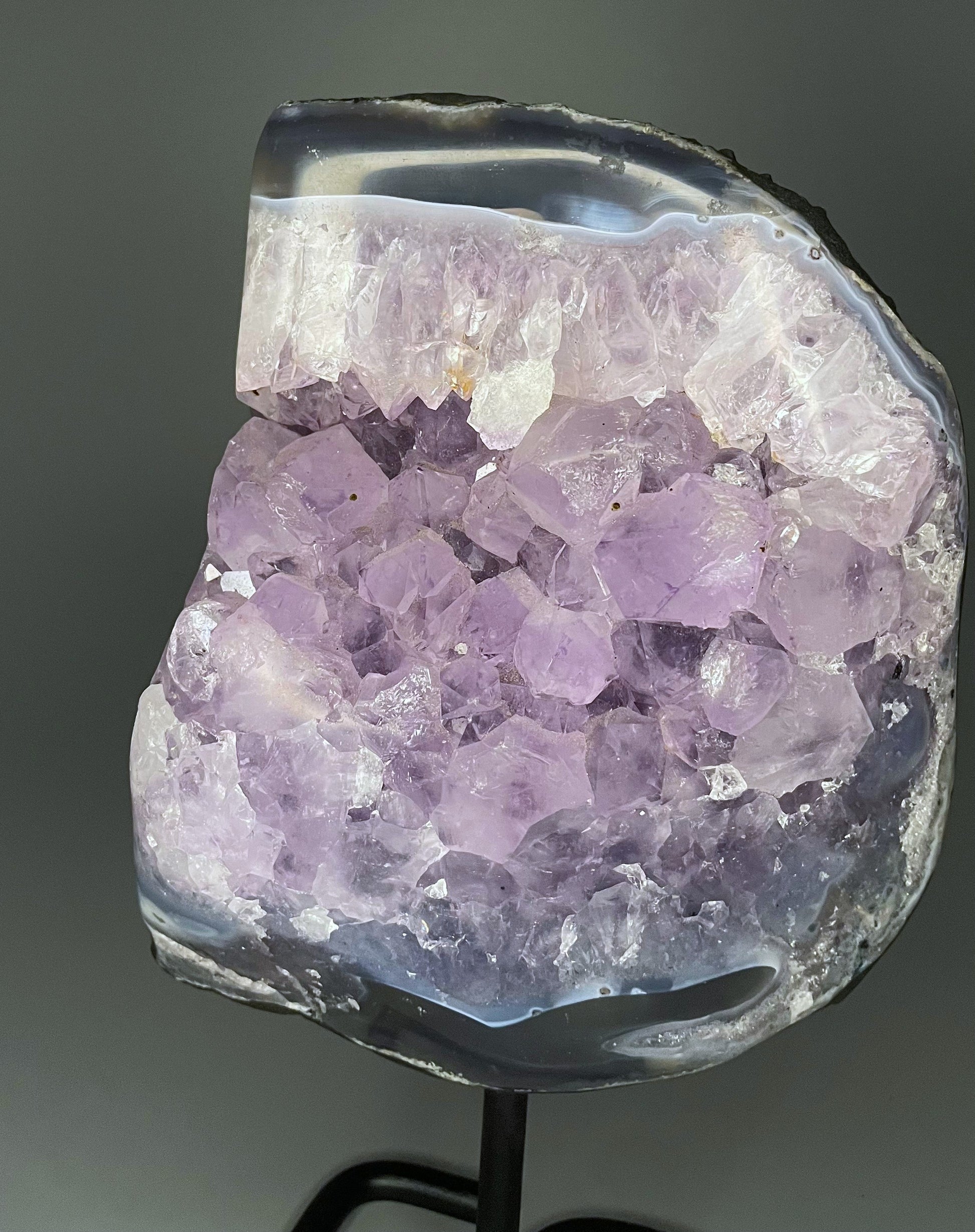 A Brazilian amethyst cluster with purple hues and large crystals on a black metal stand.