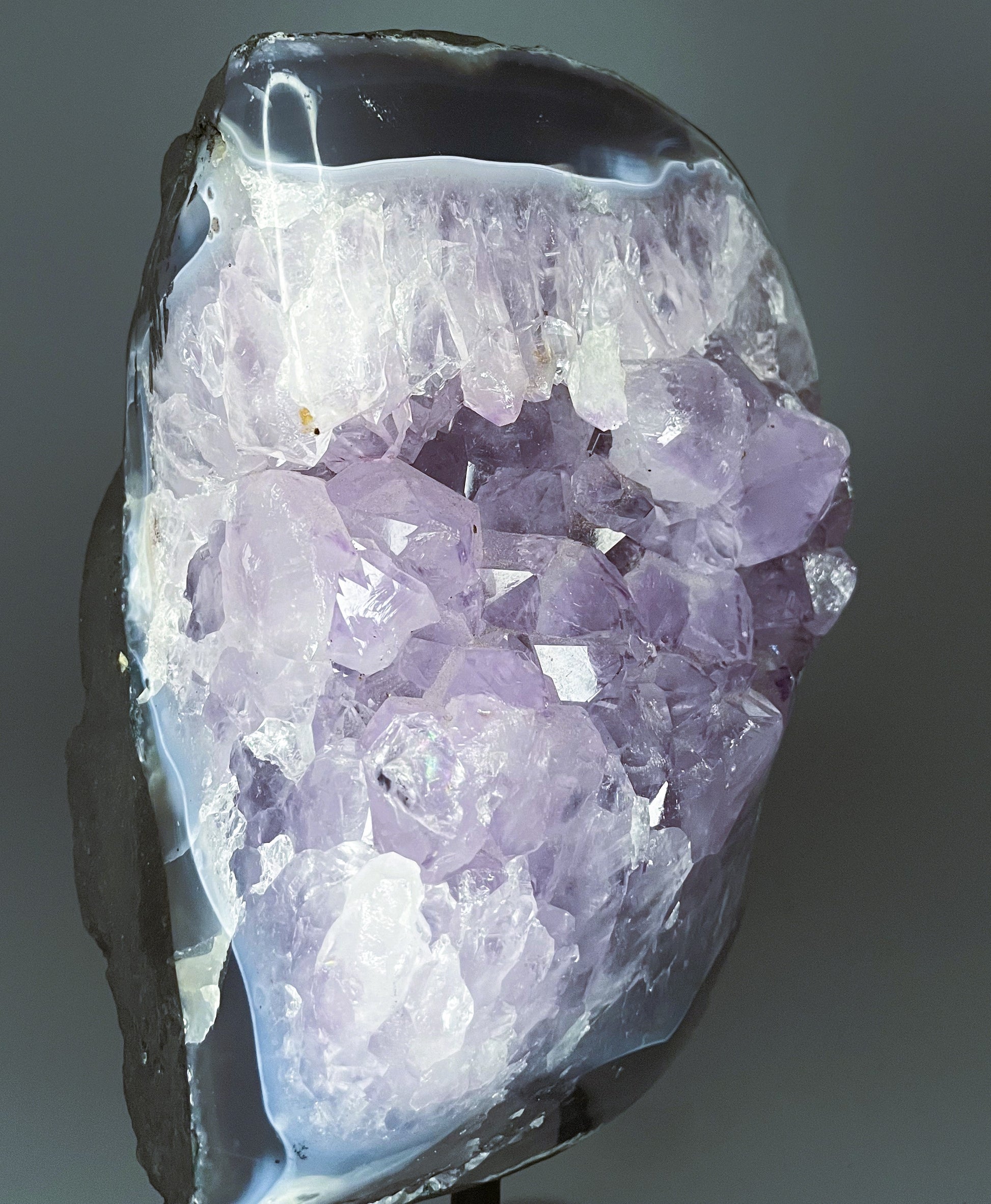 A Brazilian amethyst cluster with purple hues and large crystals on a black metal stand.